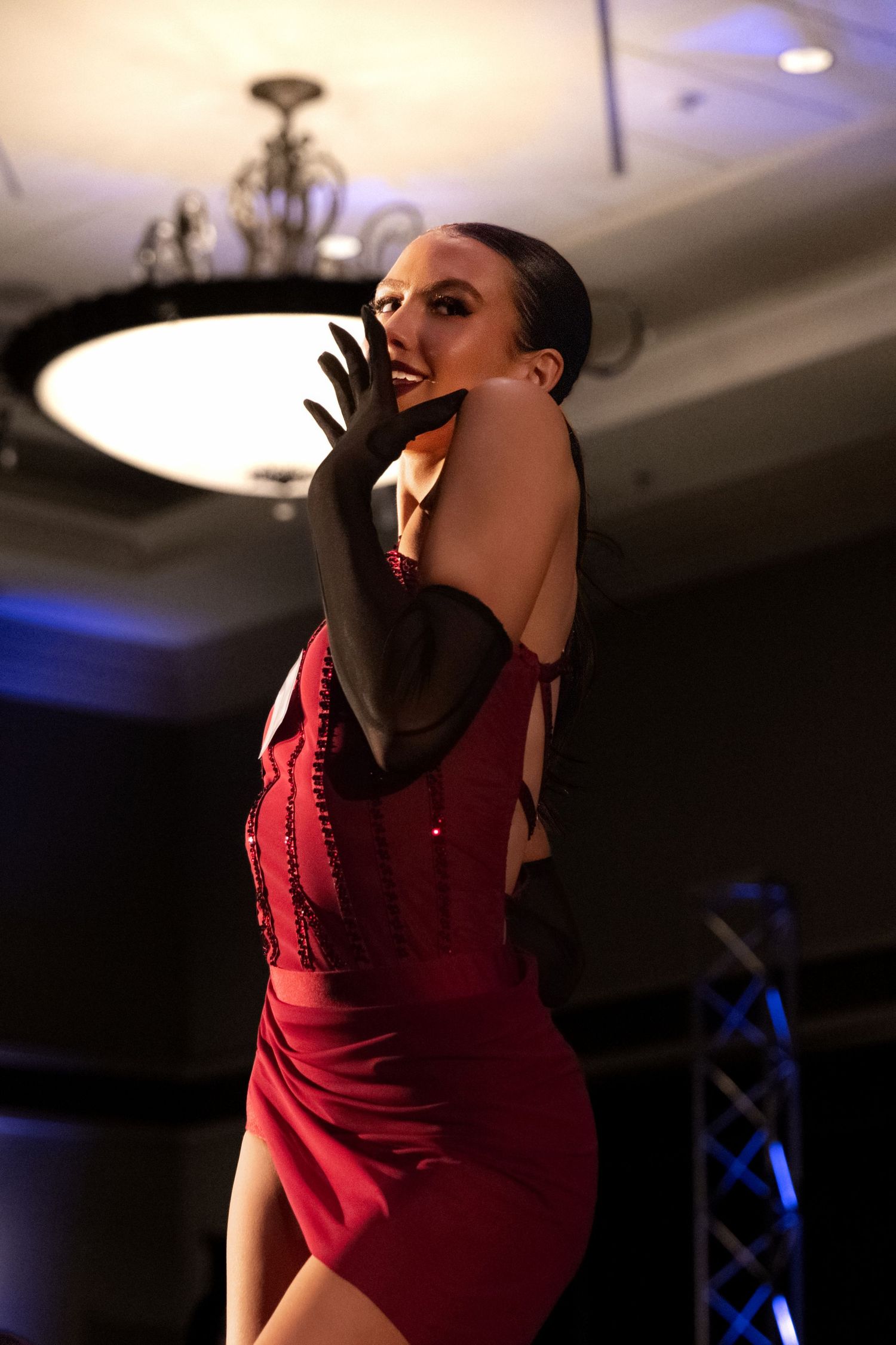 A performer in a red dress strikes dramatic poses during a stage performance under theatrical lighting.