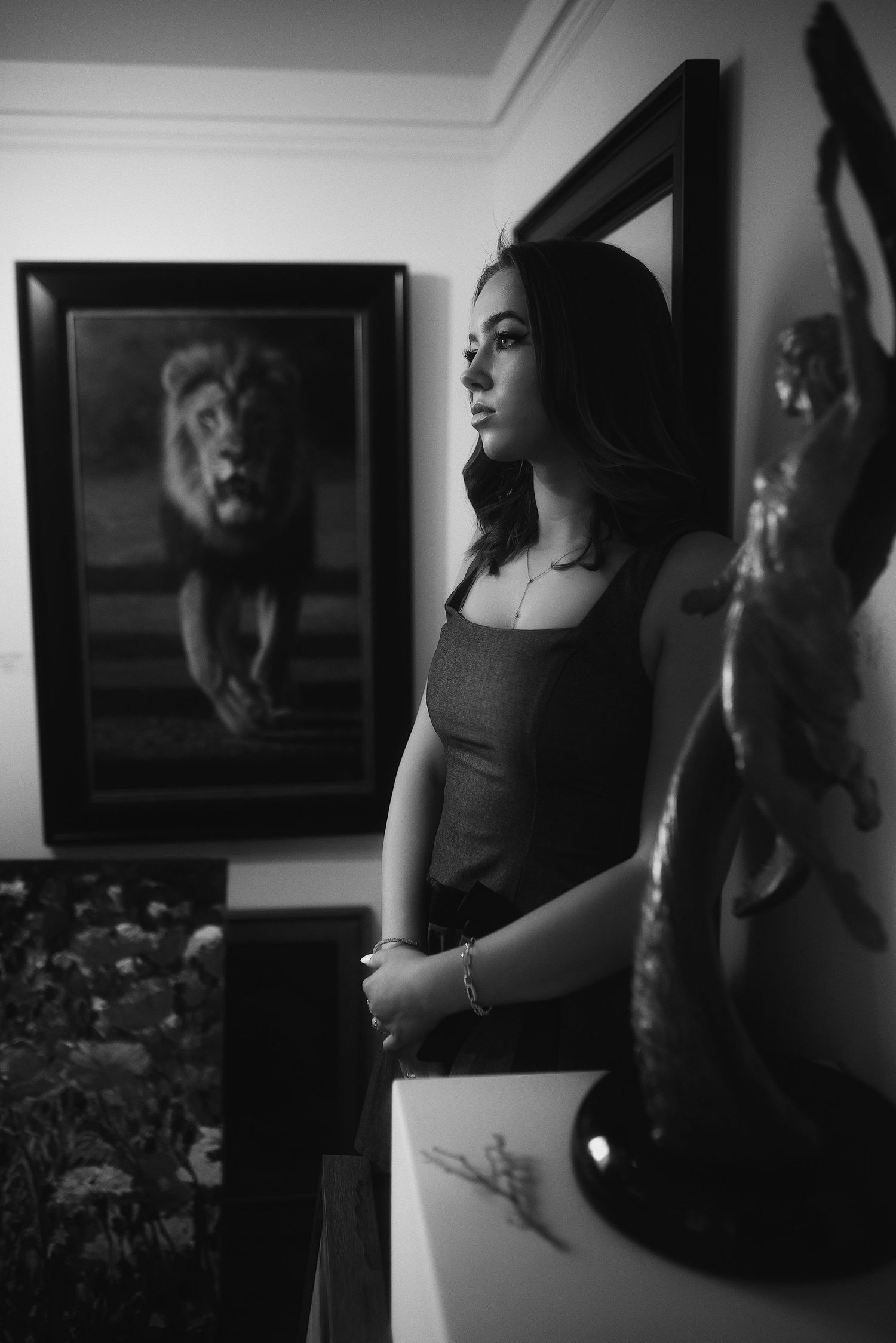 A dramatic black and white portrait in an art-filled room with a lion painting visible in the background.