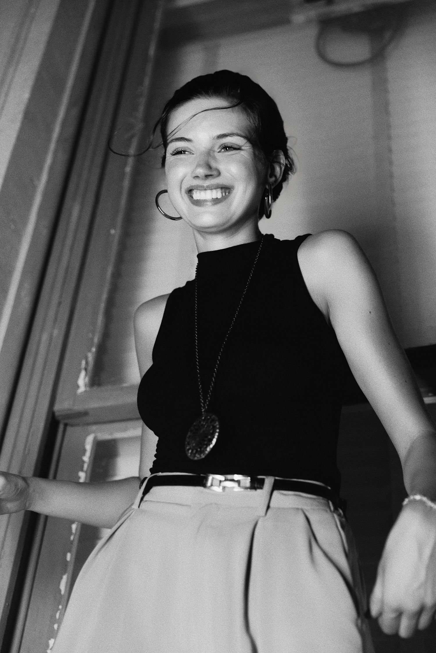 Black and white portrait photograph of a woman in a sleeveless turtleneck smiling brightly with a necklace.