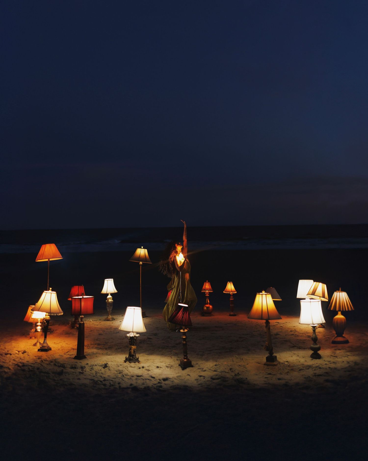 A series of glowing table lamps arranged on a dark beach at night creating a magical illuminated scene.