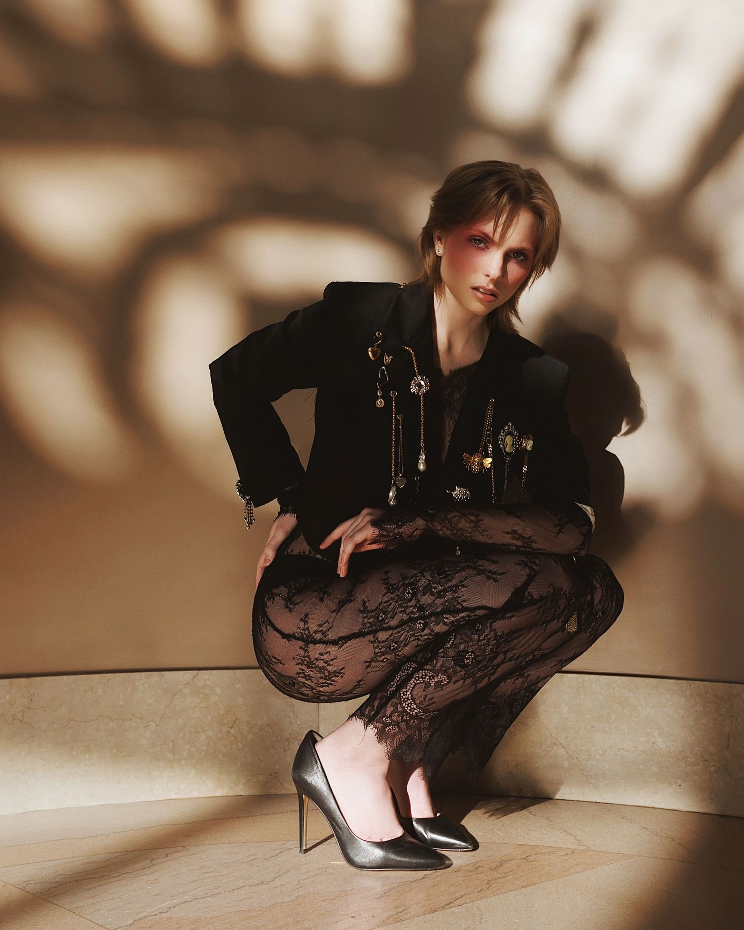Figure crouches in shadows on floor wearing black attire and heels with dramatic lighting creating artistic silhouettes.