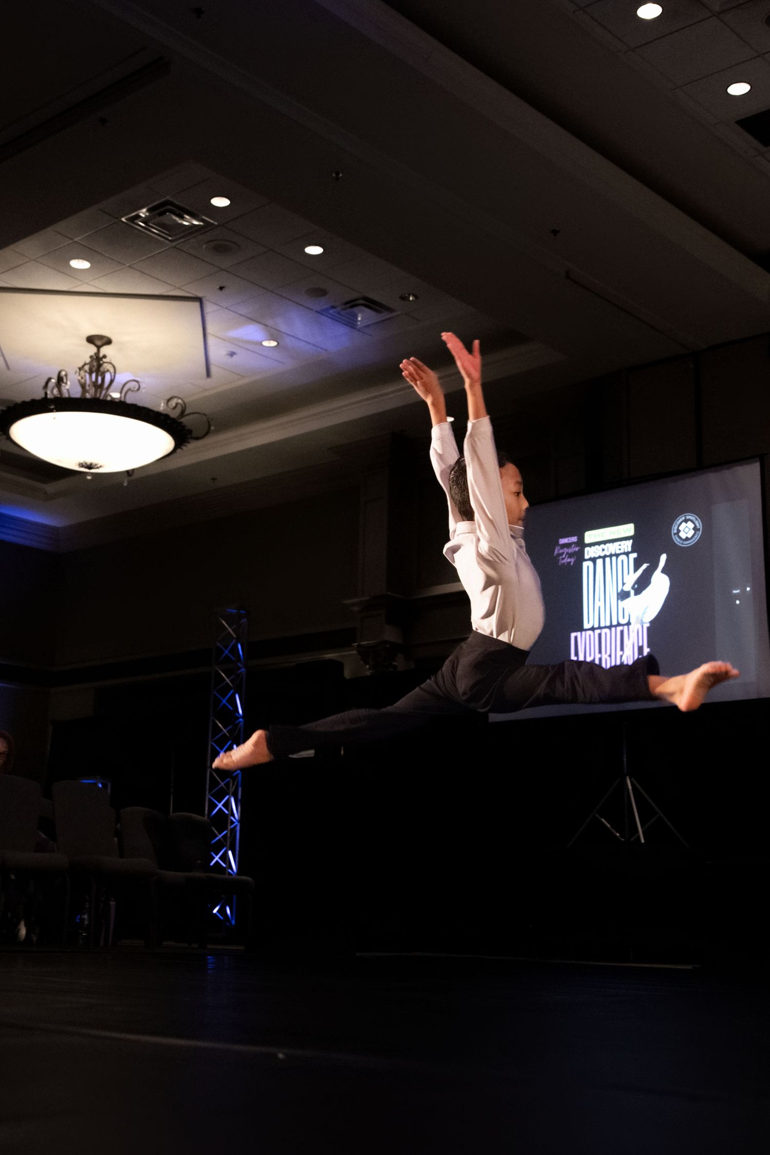 Silhouetted hands raised in a dark room with spotlights and stage lighting visible in the background.