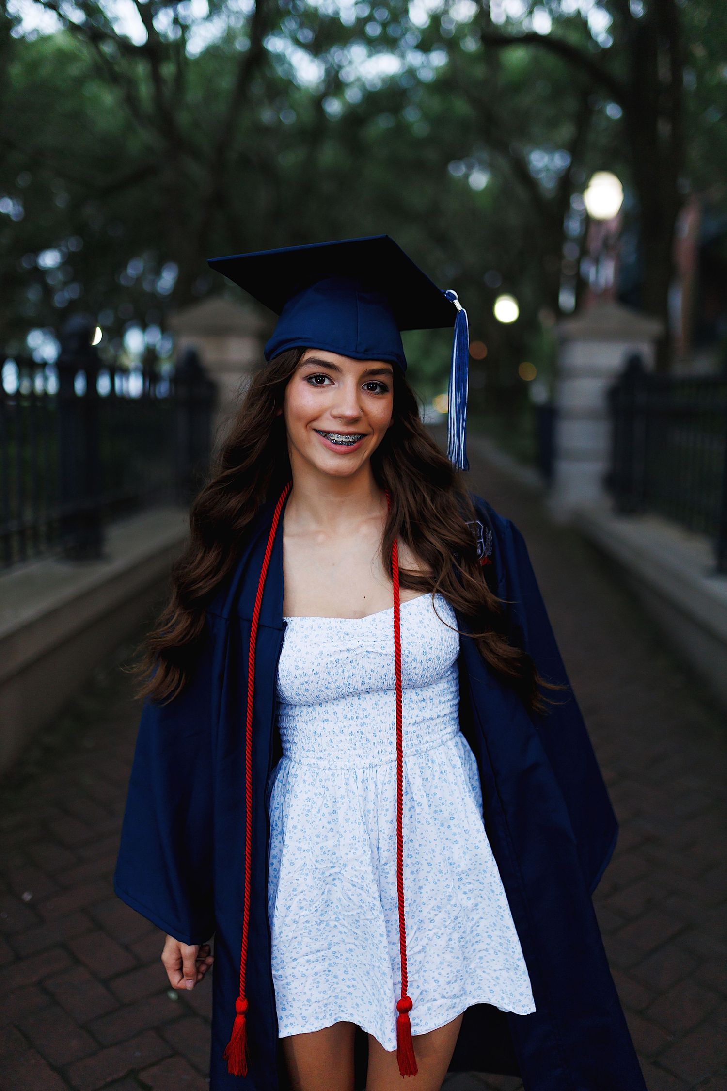 A graduate in cap and gown poses outdoors against a tree-lined path in a series of photos.