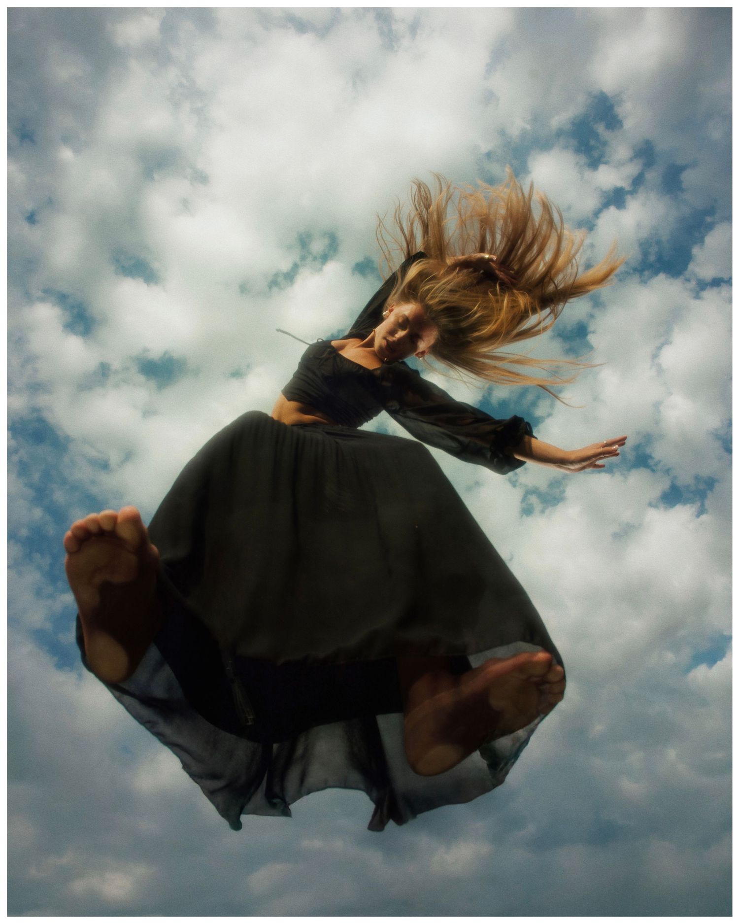 A person in a black dress floats gracefully through the air against a cloudy sky background in a dynamic photo sequence.