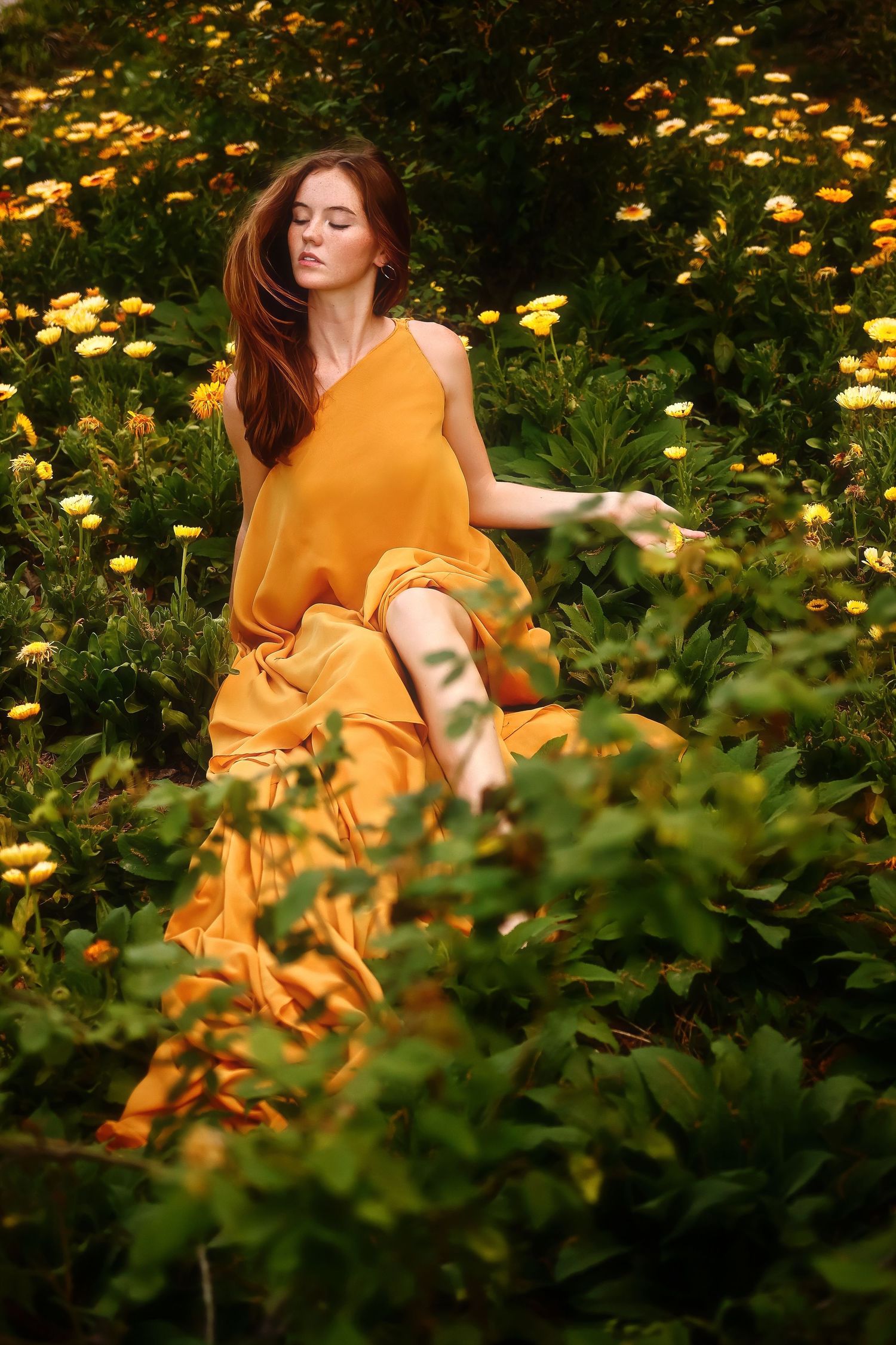 A figure in a flowing yellow sundress reclines gracefully among blooming yellow wildflowers in a garden setting.