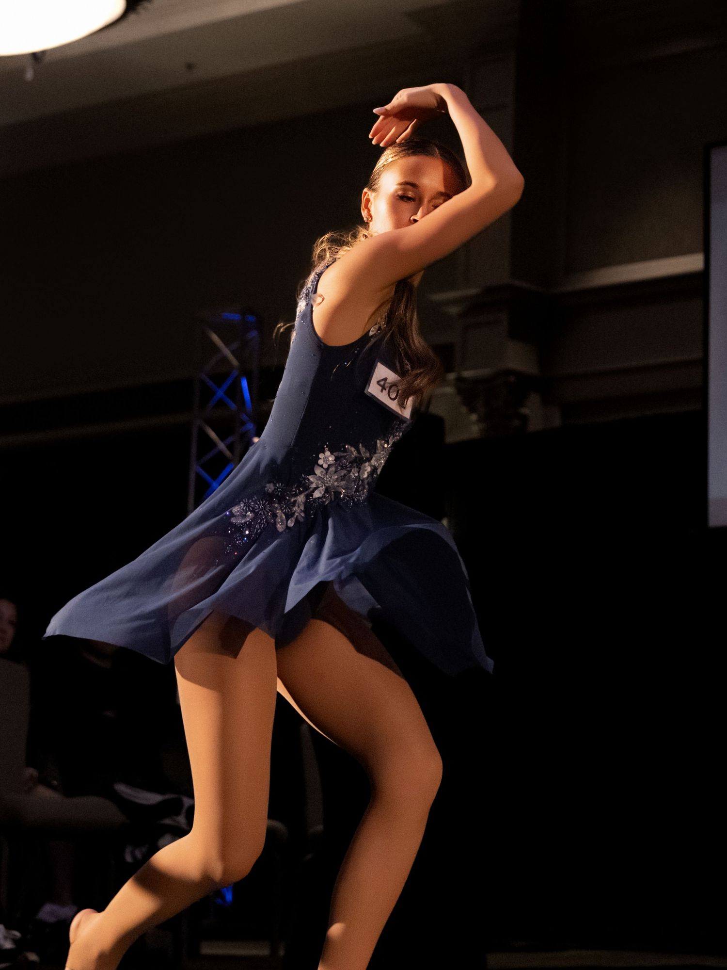 A dancer performs a dynamic leap in a navy blue costume against a dark background during a stage performance.