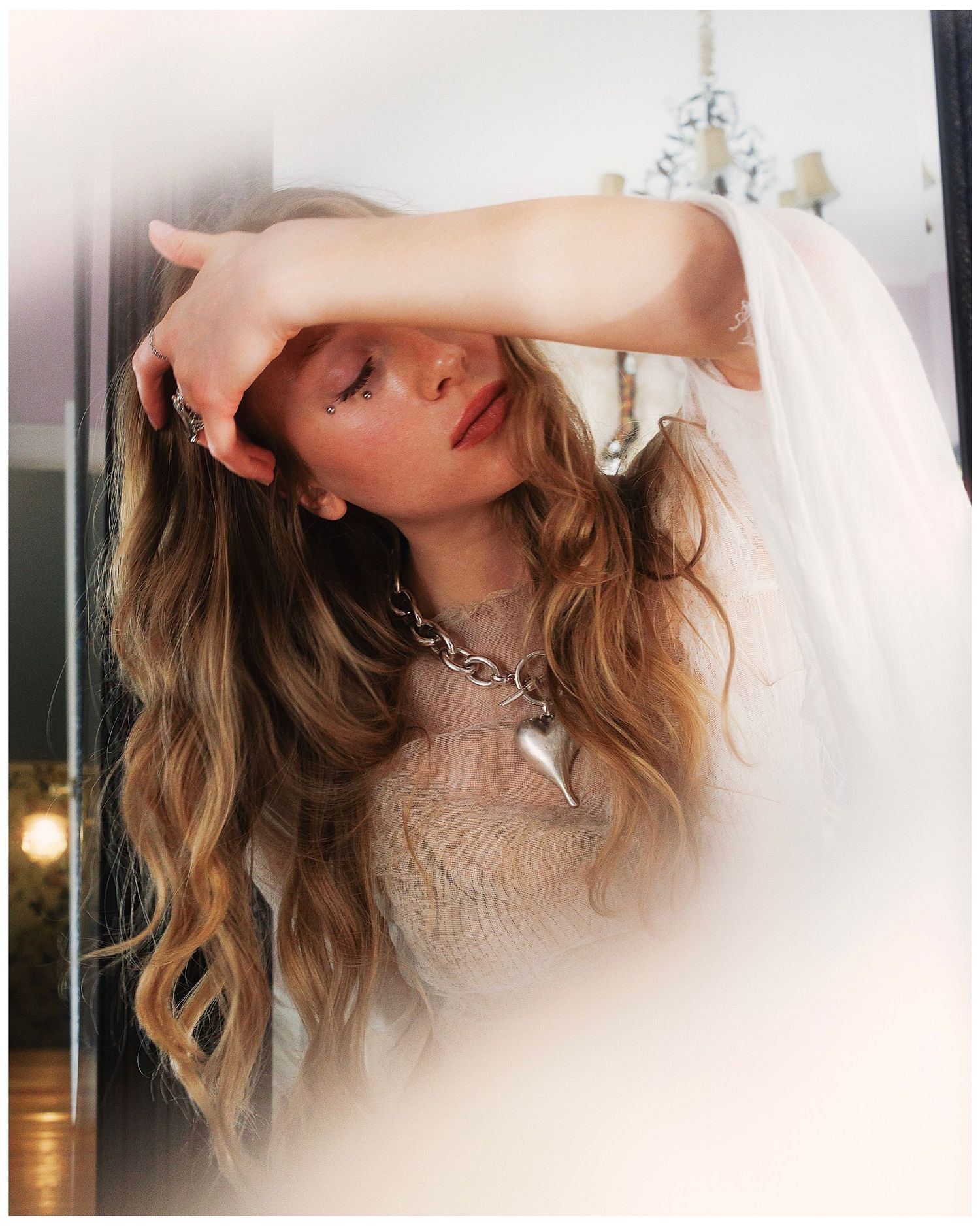 A model poses in dramatic lighting wearing lace and a silver chain necklace, creating ethereal fashion portraits.