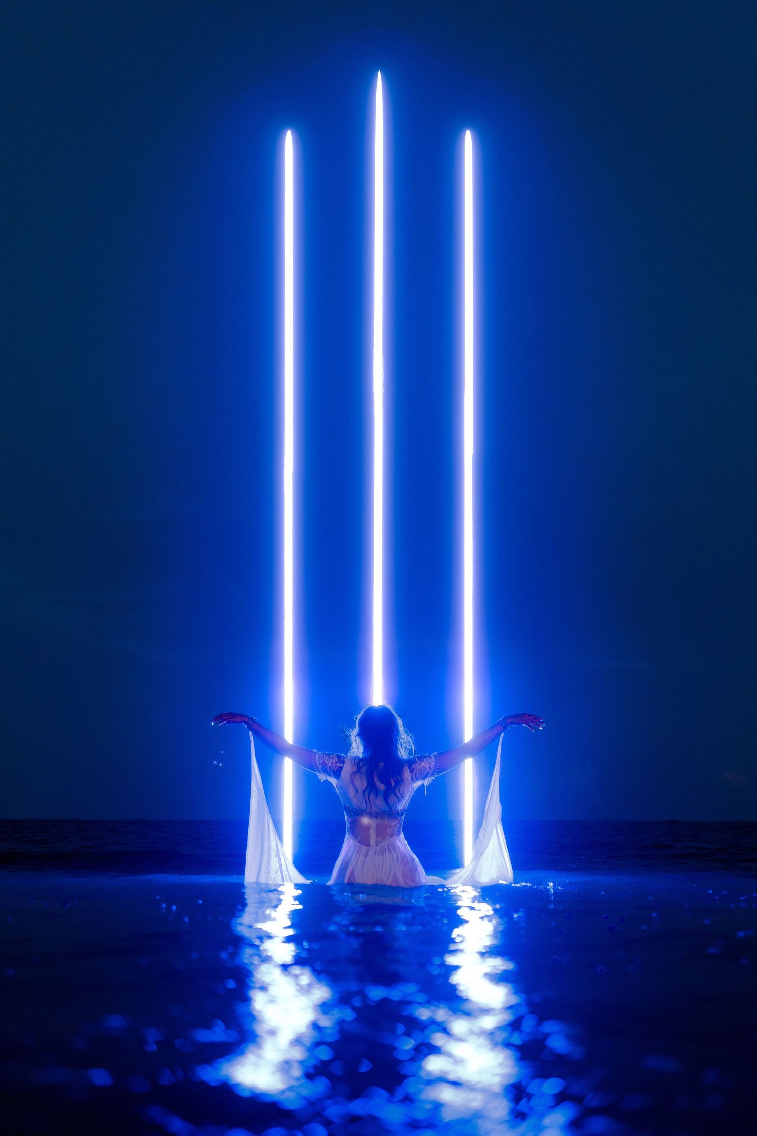 A figure stands between glowing vertical blue light beams creating a dramatic nighttime scene outdoors.