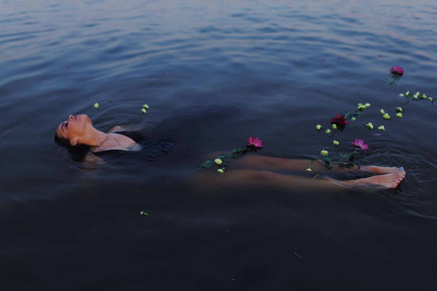 Person floating peacefully in dark water surrounded by glowing neon lights creating an ethereal nighttime scene.