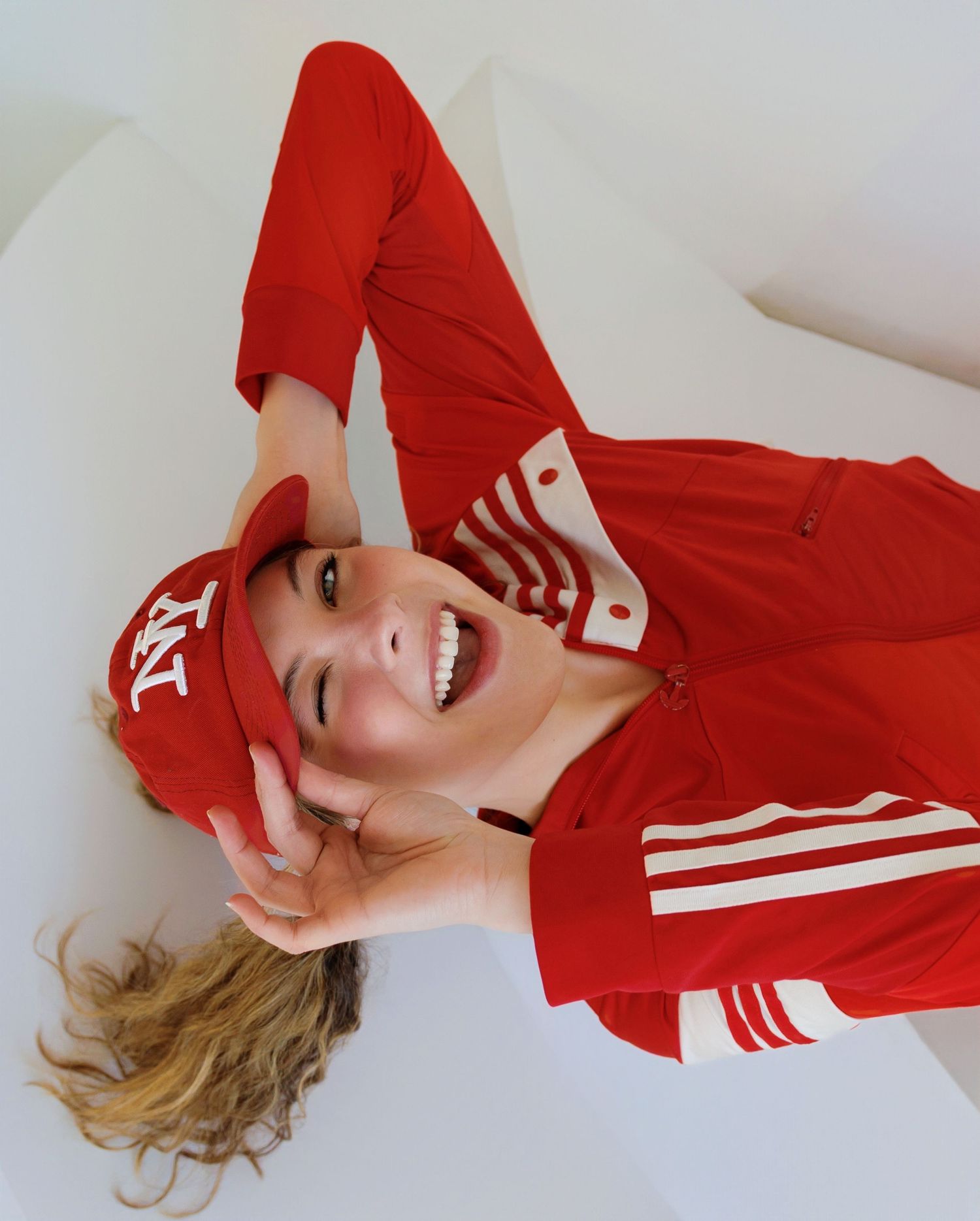 Person in red athletic wear lies on white background with joyful expression and dynamic pose.