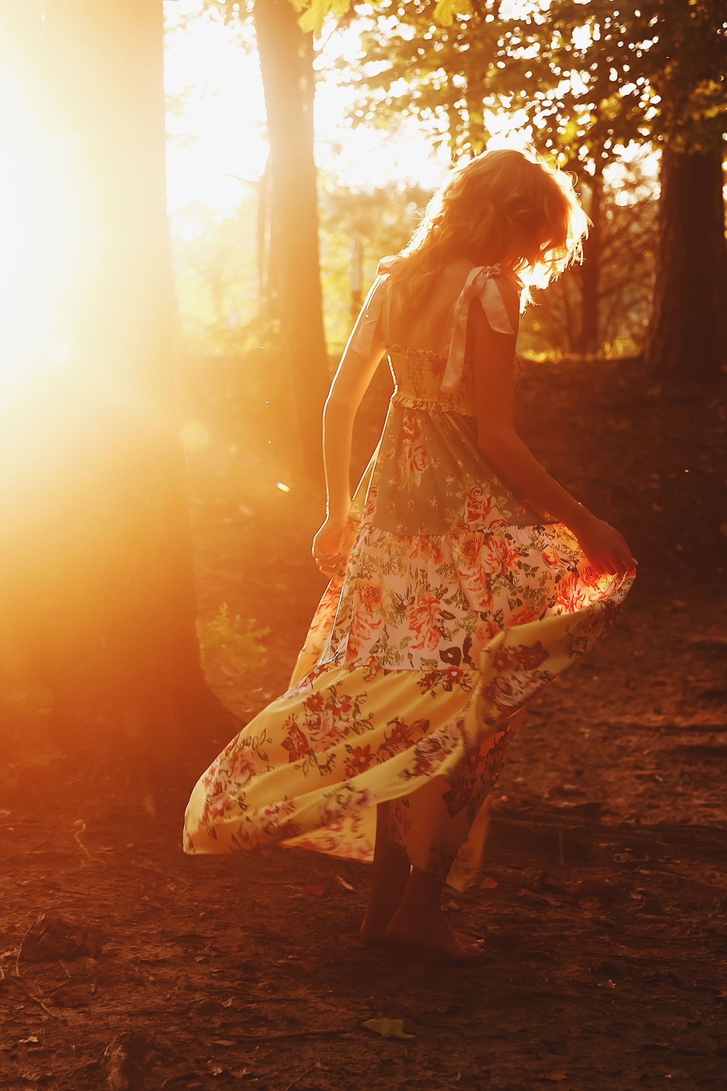 A person in a floral dress twirls in a dreamy golden sunset forest setting, creating a magical ethereal atmosphere.