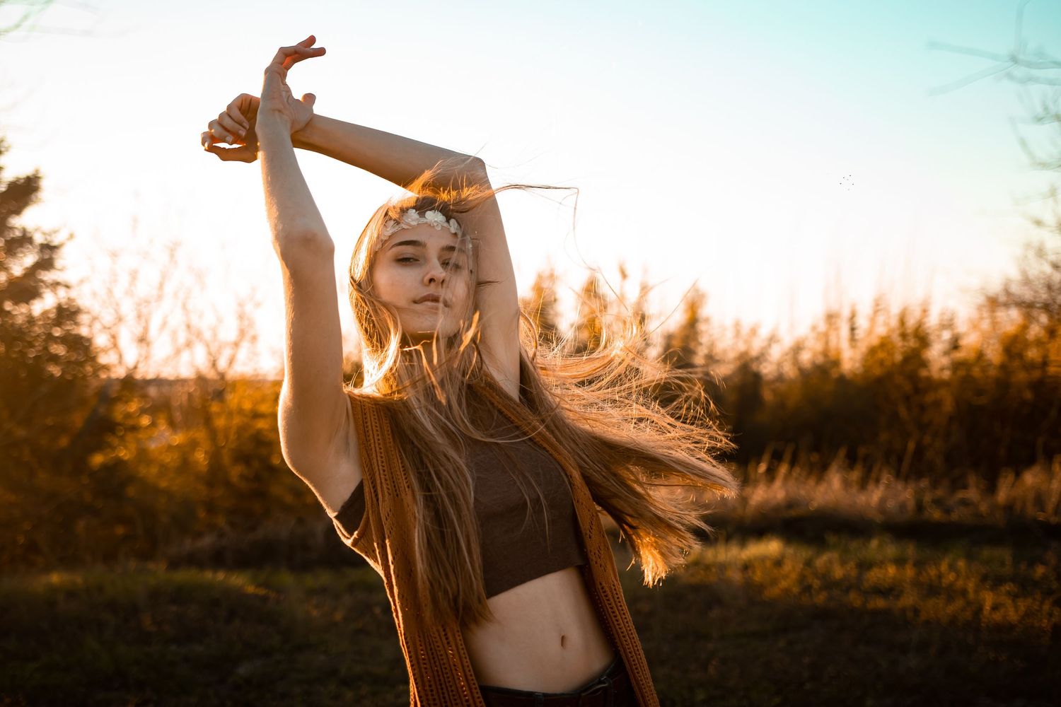 A silhouetted figure stands with raised arms against a warm sunset sky with trees in the background.