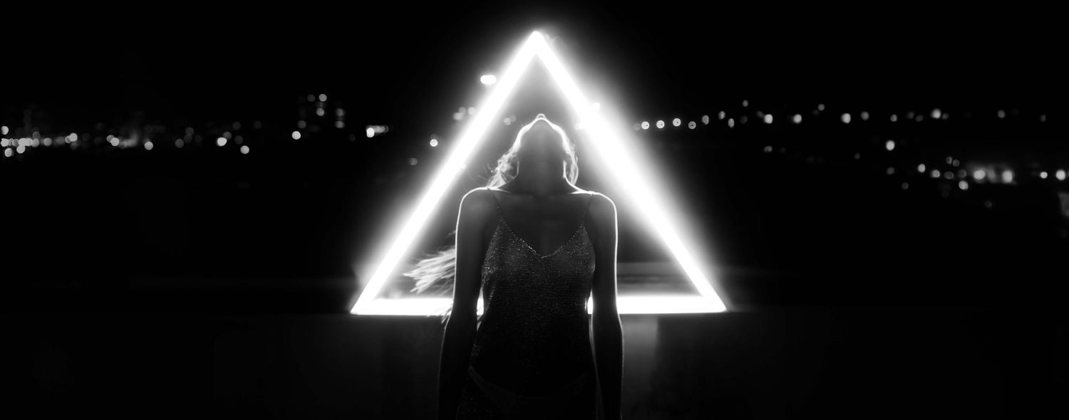 A silhouetted figure stands between glowing triangular shapes against a dark background.