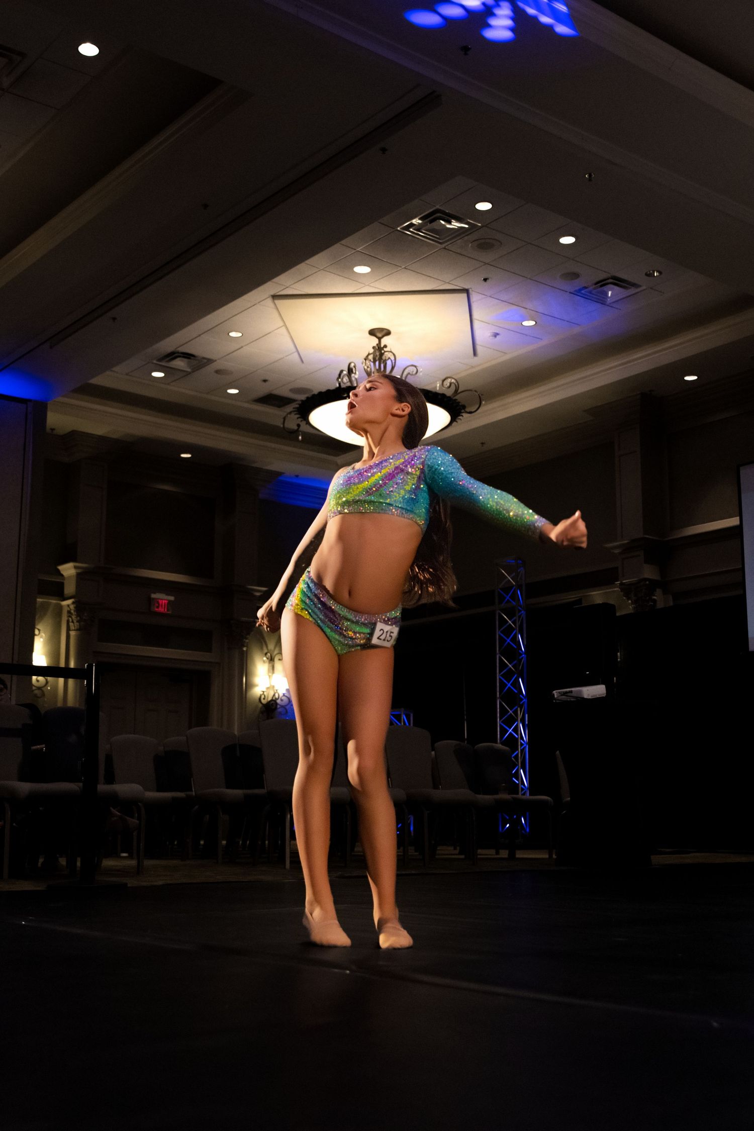 Dancer performing an acrobatic backbend move on a dimly lit stage with blue lighting effects in the background.