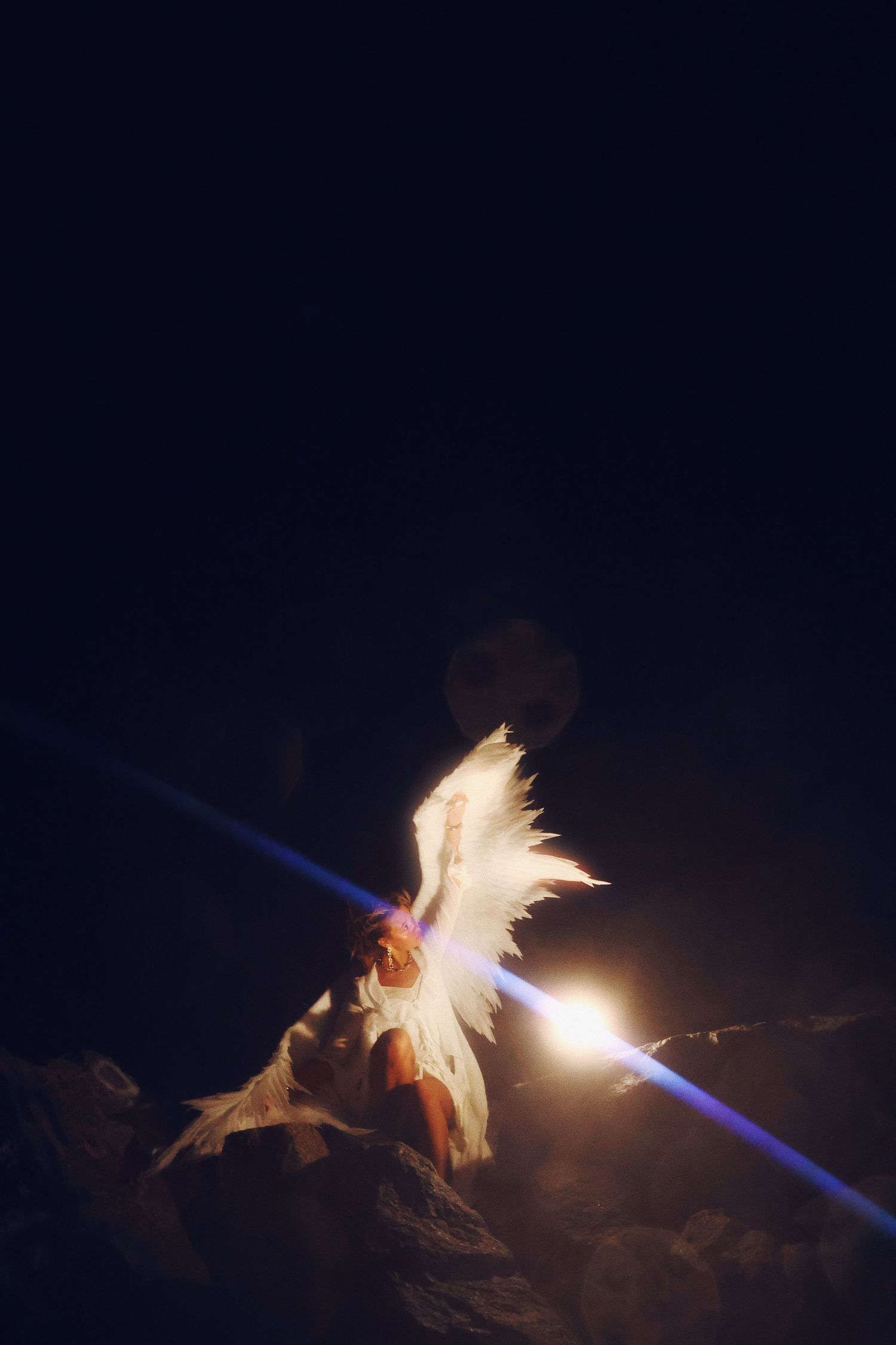 A bright light beam illuminates a dramatic rock formation against a dark night sky with a glowing effect.