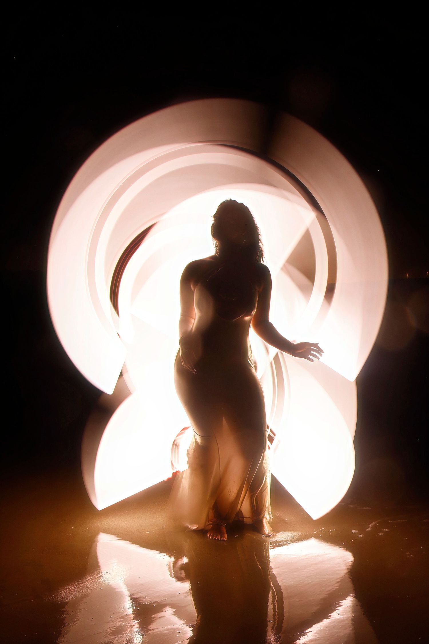 A silhouetted figure performs light painting with glowing trails creating circular patterns against a dark background.