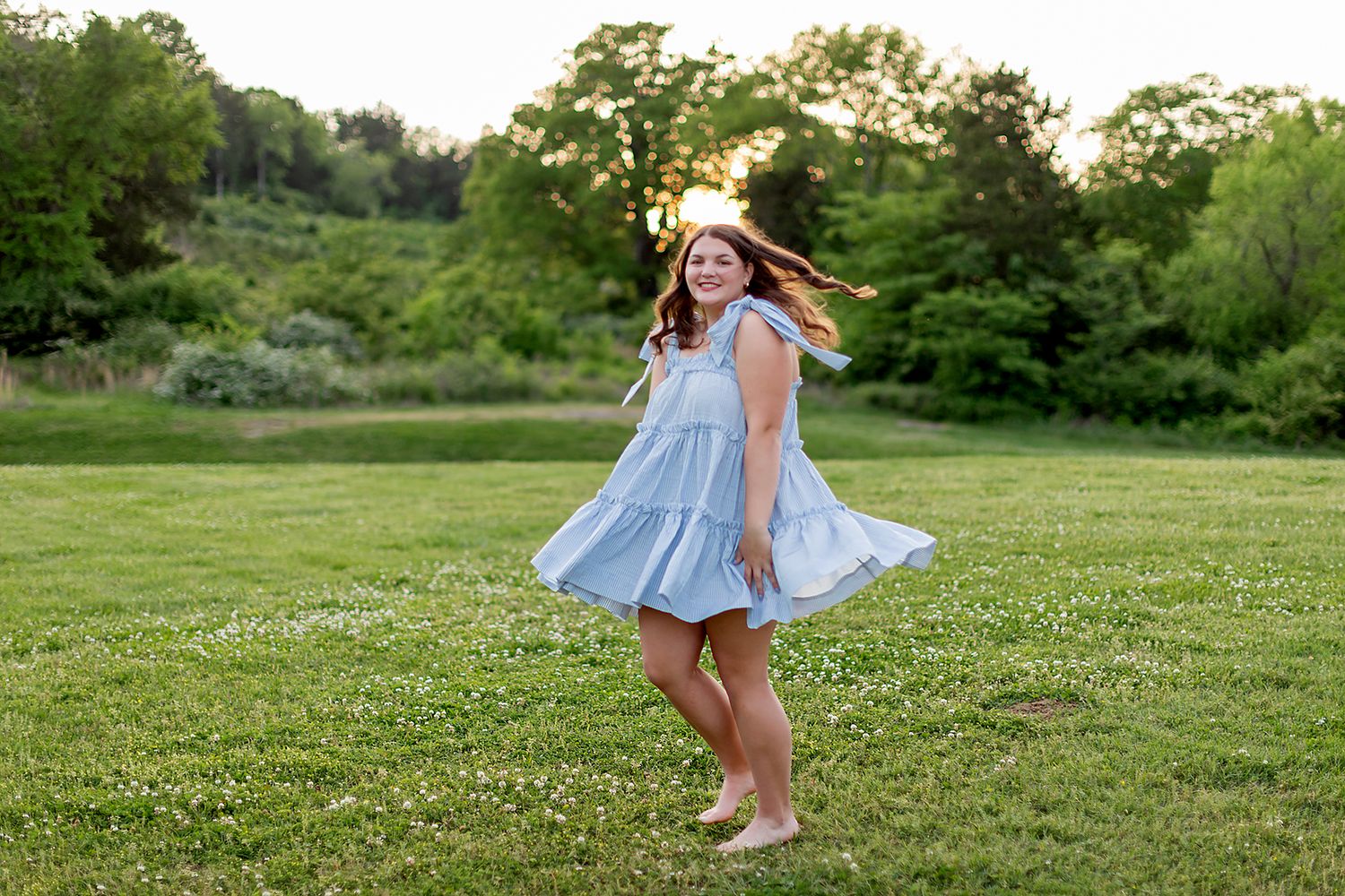 Girl twirling in blue dress while playing in green summer field. Senior pictures by MegMc Photography.