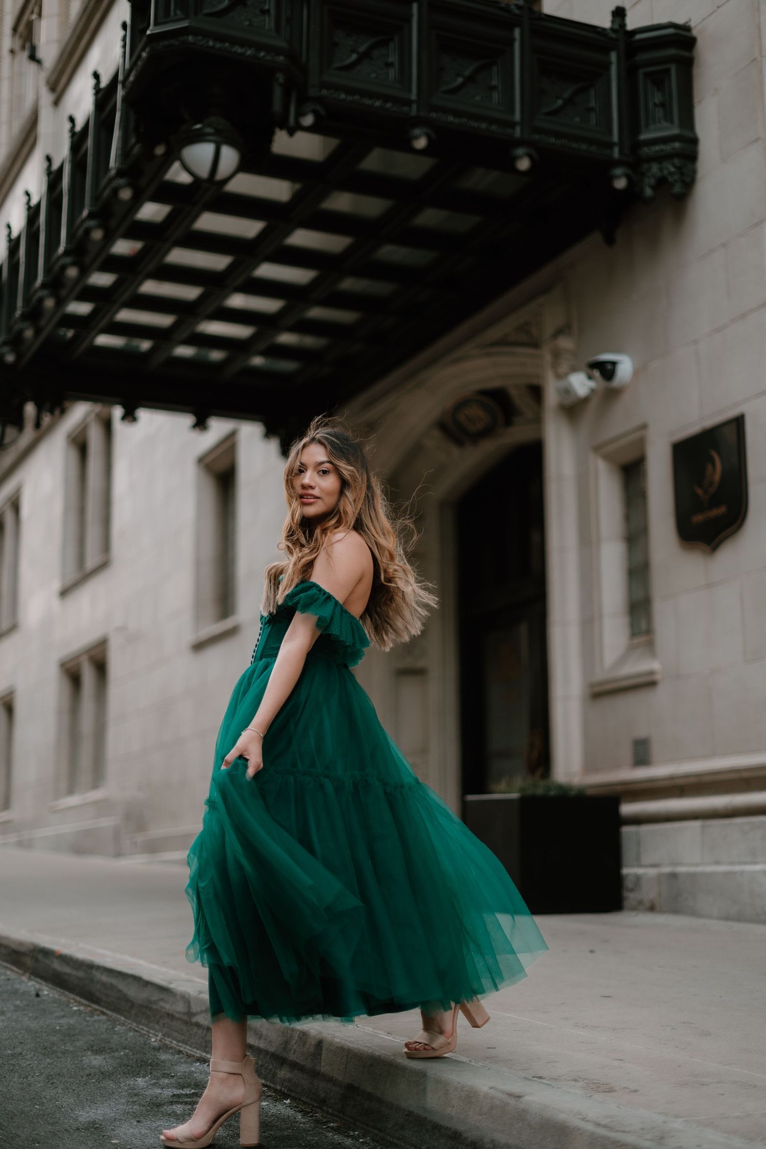 A woman wearing an elegant emerald green tulle dress twirls in front of a historic building entrance.