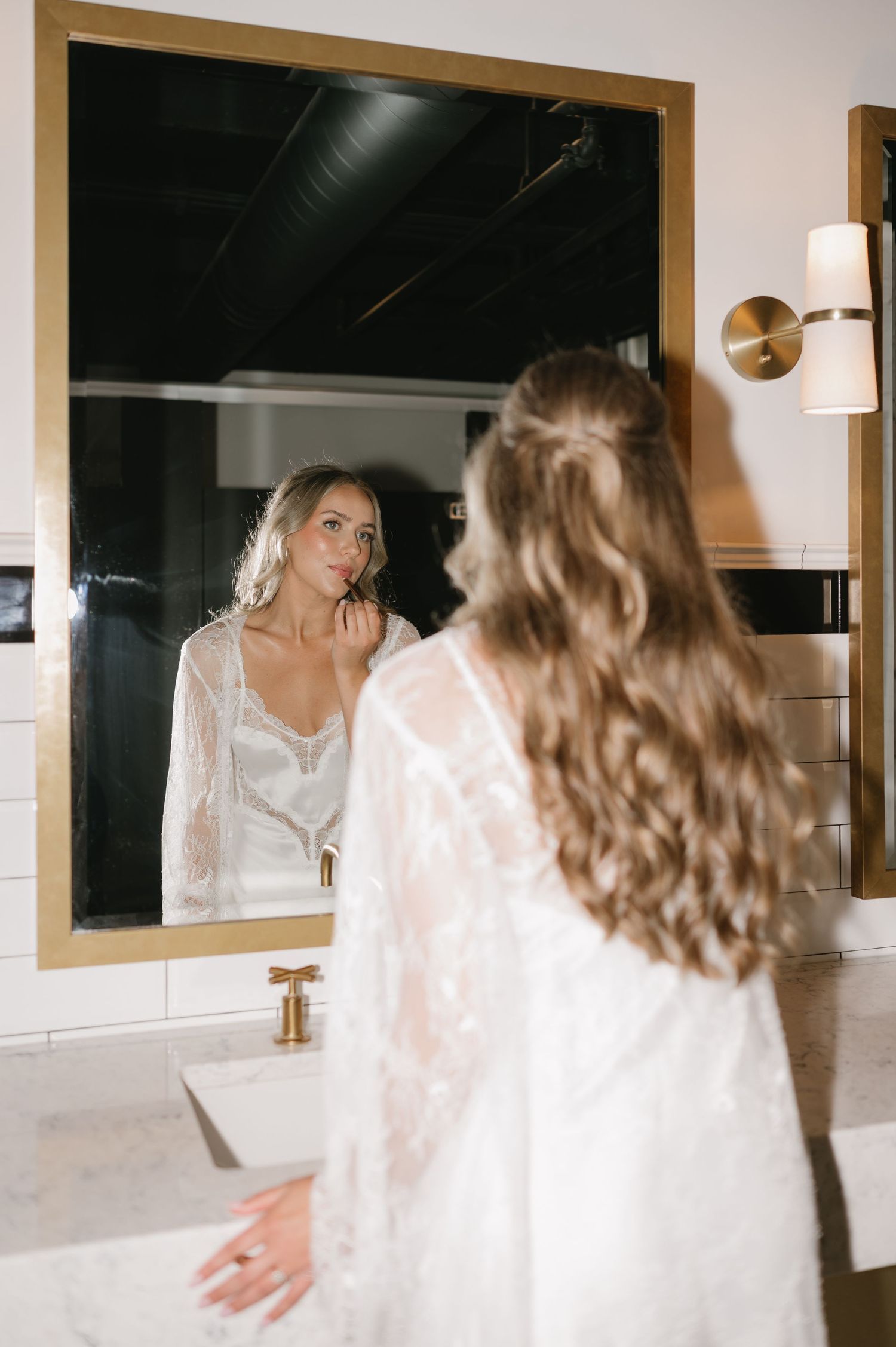 A romantic reflection in a bathroom mirror shows a woman wearing white lace lingerie and a sheer robe.