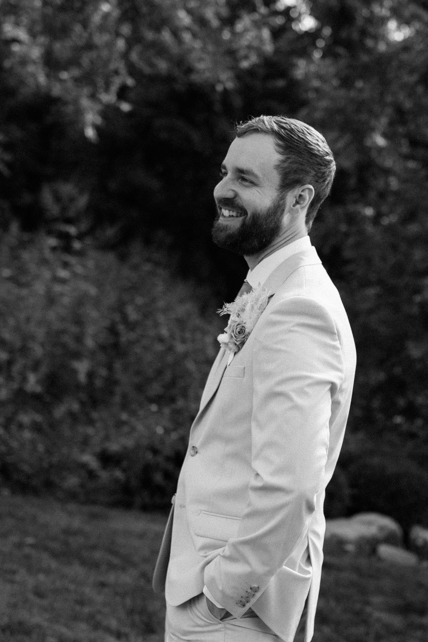 A joyful moment captured in black and white of someone wearing a light colored suit and boutonniere at an outdoor event.