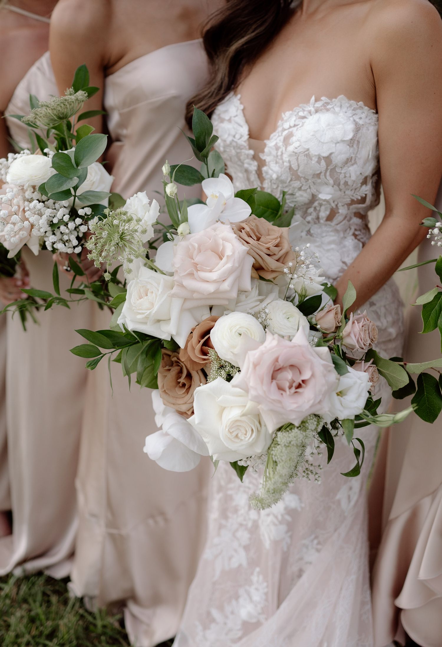 Close-up of blush and white wedding bouquets with roses and eucalyptus against bridesmaid dresses in champagne hues.