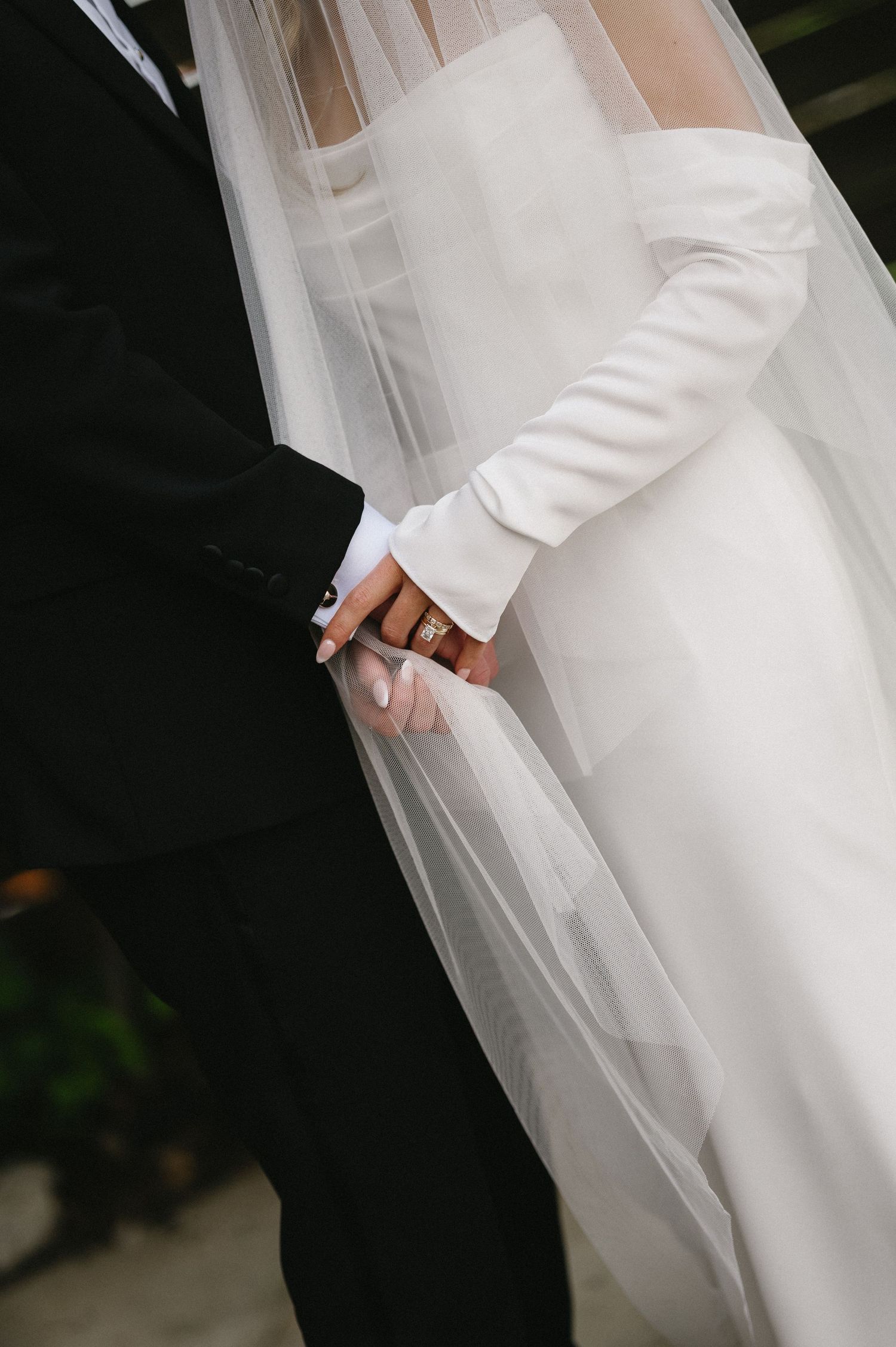 Elegant bridal gown detail showing flowing white satin and sheer veil against dark background.