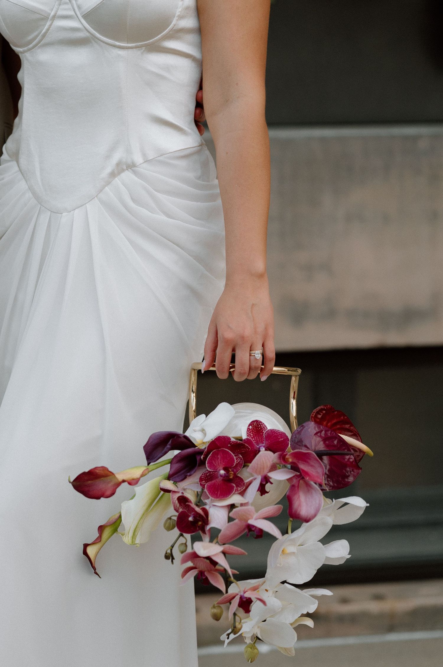 Close-up view of elegant white wedding dress with bustier detail and cascading orchid bouquet in pink and white tones.