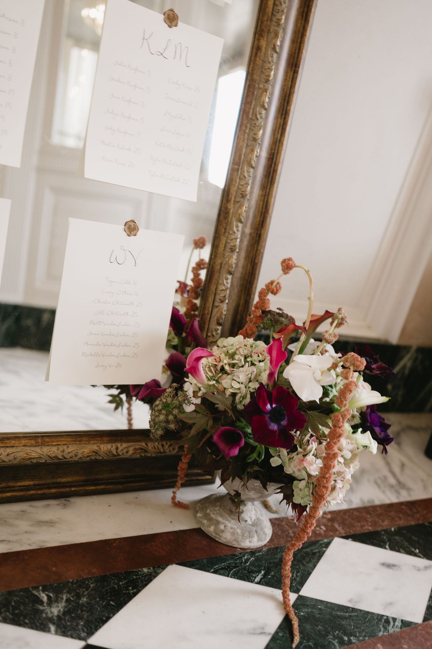 A vintage gold frame mirror with white papers displayed above and a colorful floral arrangement in a vase on marble surface.