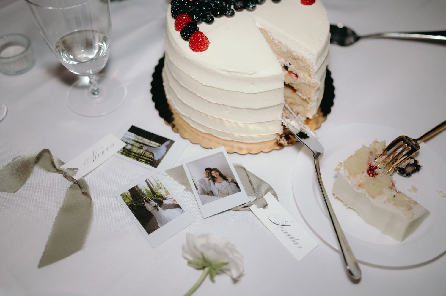 White wedding cake slices being served on plates with red decorative berries and green garnish.