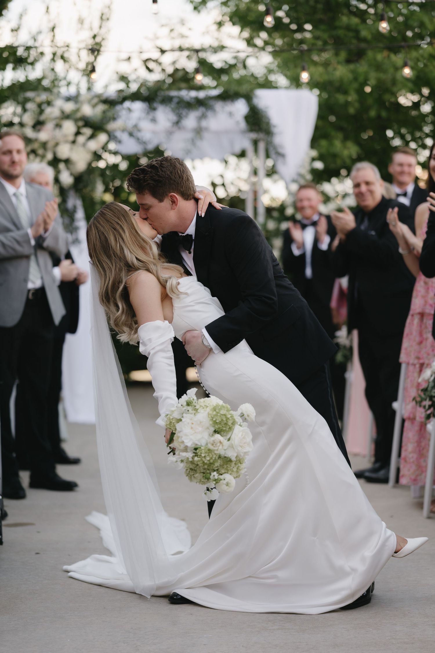 A couple performs an elegant dip during their first dance at an outdoor wedding reception while guests watch.