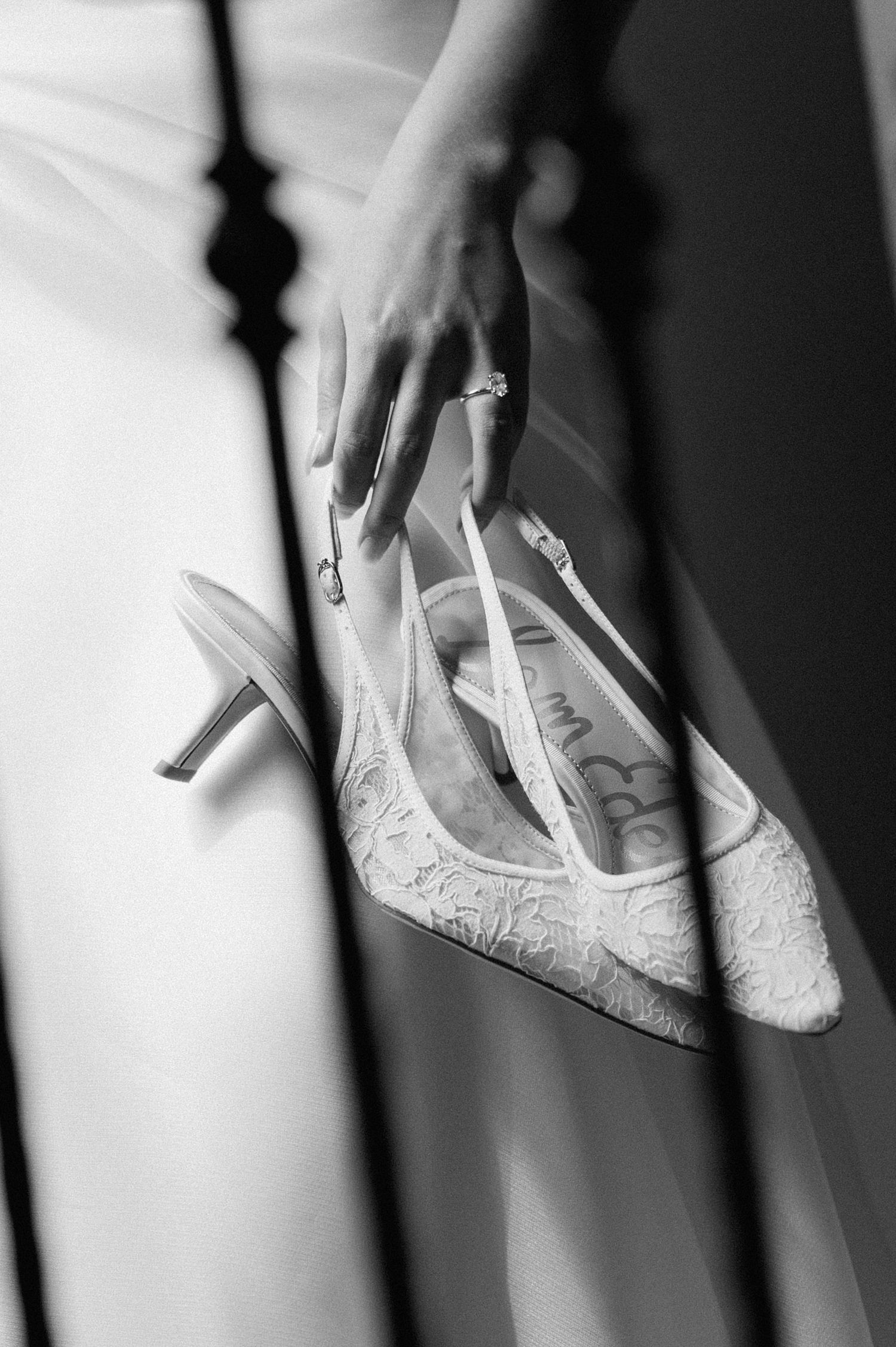 Elegant white lace bridal ballet flats being held against a soft black and white background.