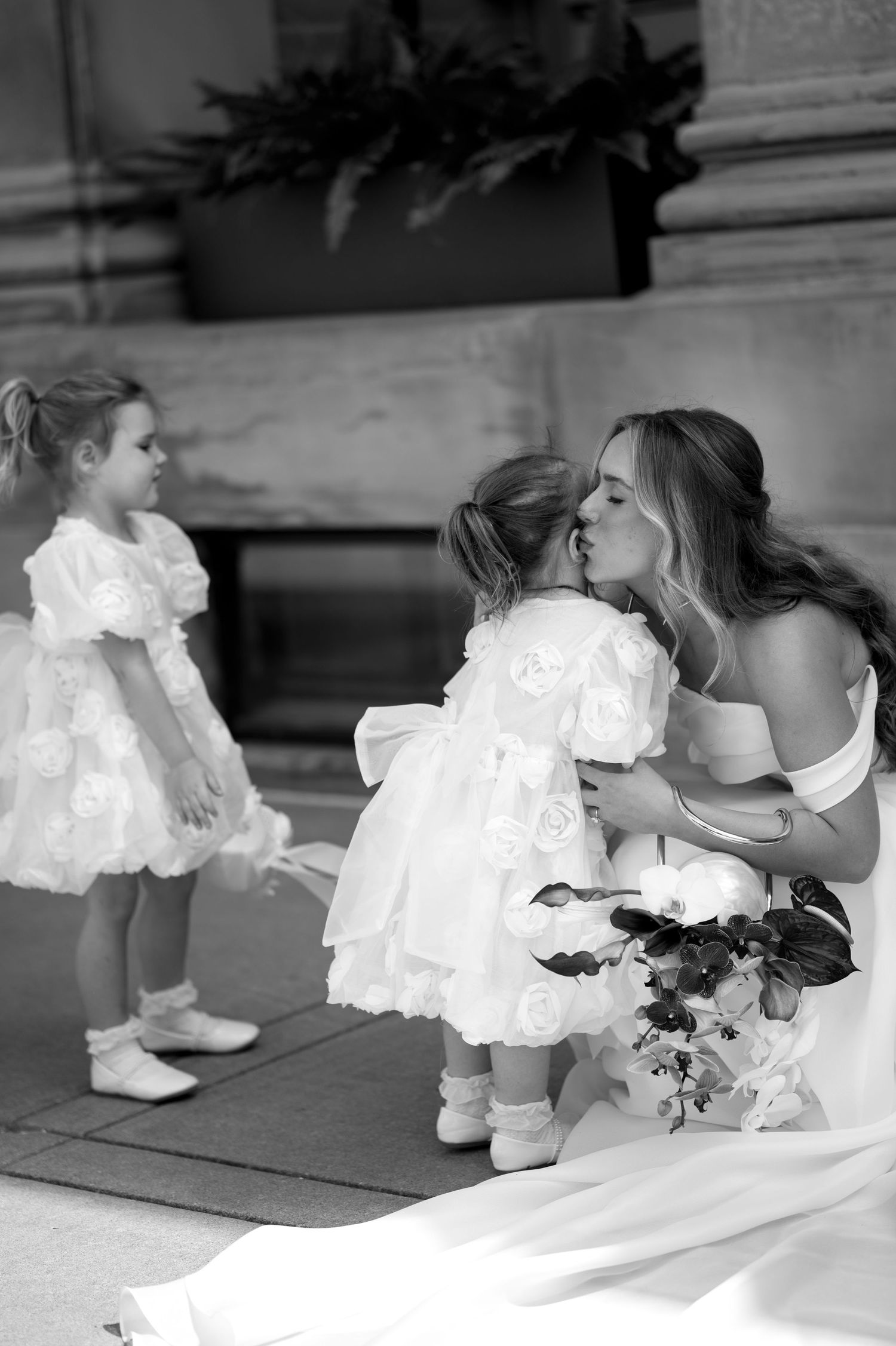 Black and white wedding photograph shows small children in white lace dresses with the bride on outdoor steps.