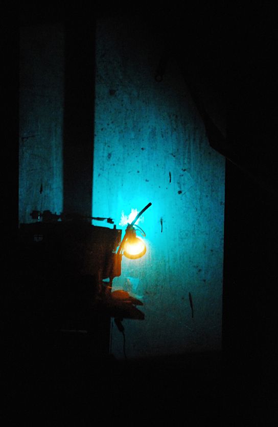 Leuchtende Vintage-Lampe an türkiser verwitterter Wand in der Dunkelheit, atmosphärische Nachtaufnahme mit warmem Licht