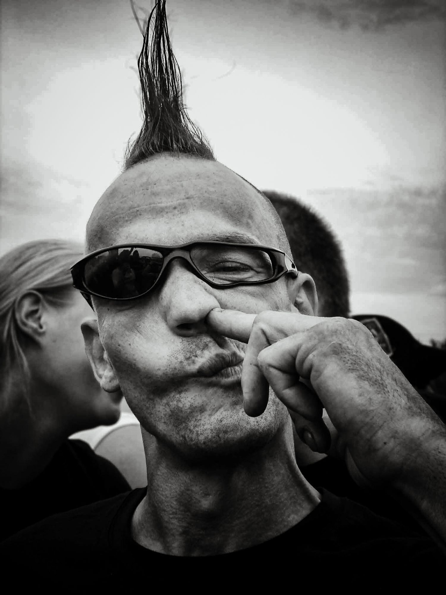 Charakterporträt von Jenny Jacoby: Punker mit Irokesenschnitt und Sonnenbrille in nachdenklicher Pose, Schwarz-Weiß-Fotografie.