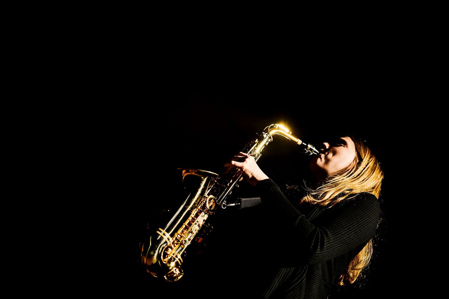 Saxophonistin im Bühnenlicht, fotografiert von Jenny Jacoby – ausdrucksstarkes Musikerporträt mit goldenen Lichtreflexen.