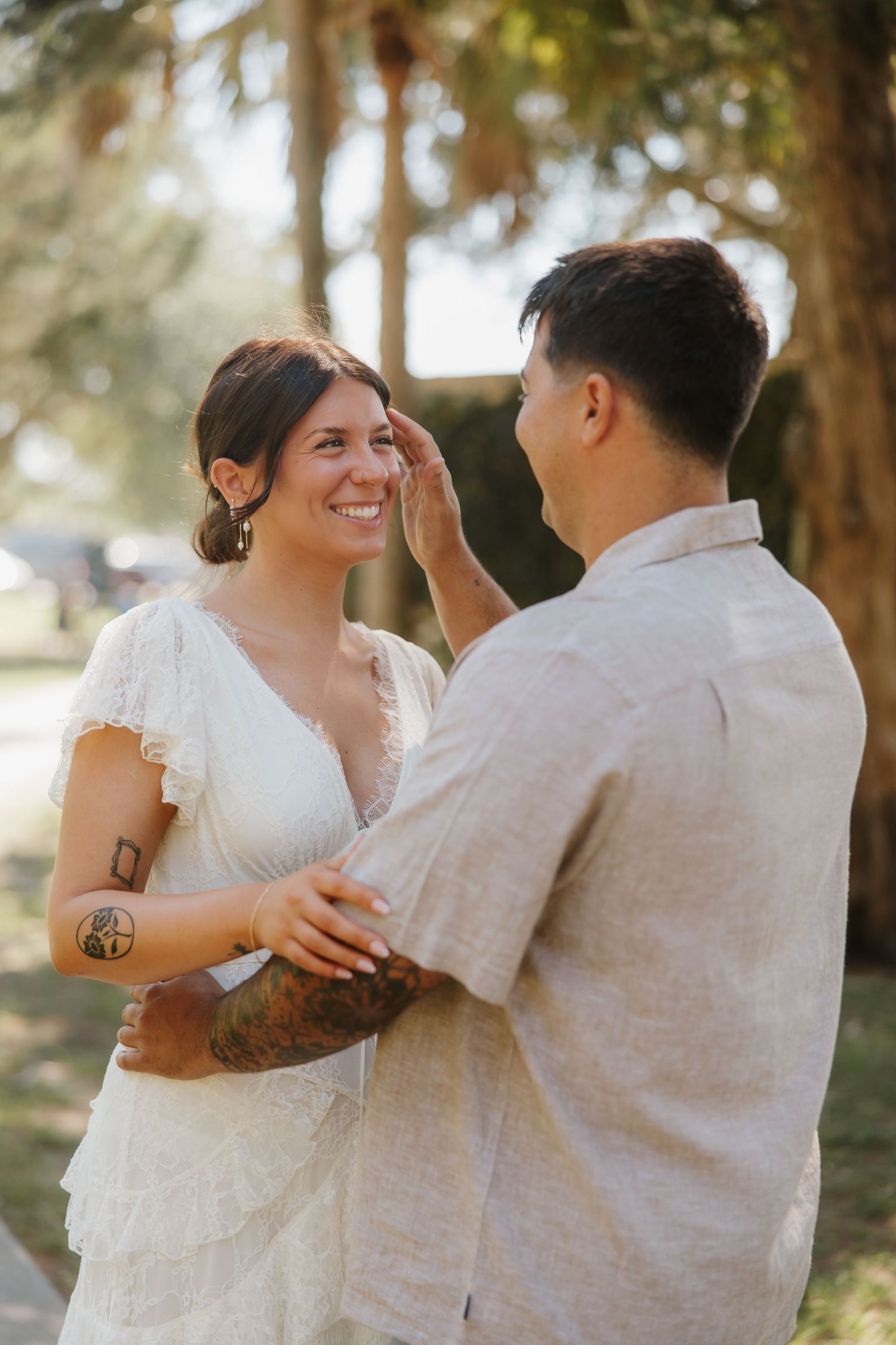 Groom tenderly brushing bride's hair during outdoor wedding ceremony.