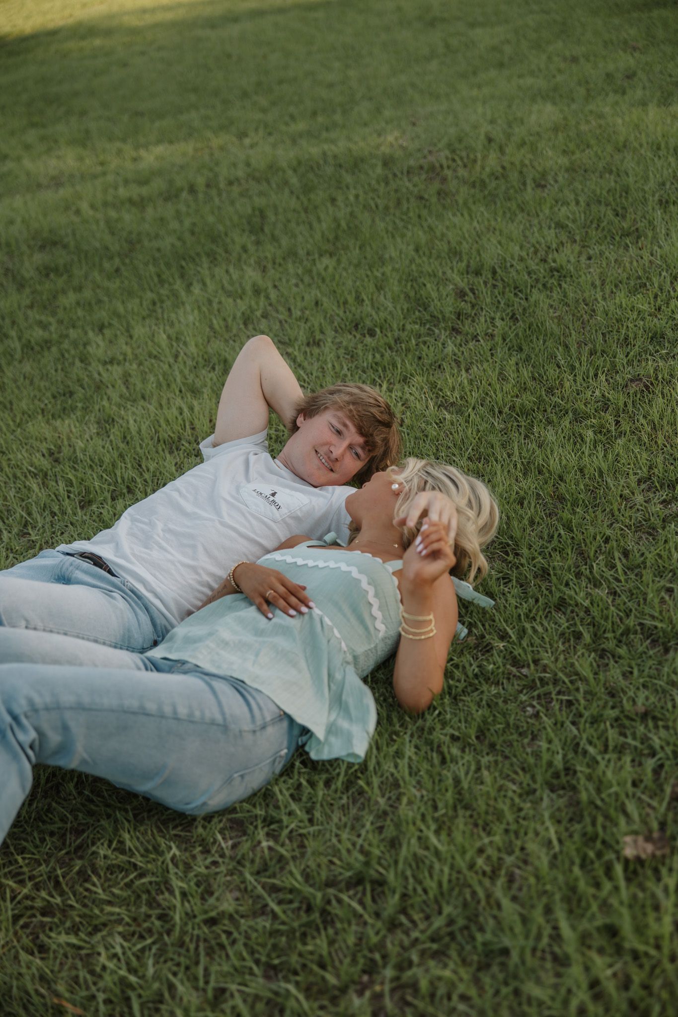A woman and child lying on green grass, smiling and relaxing together outdoors on a sunny day.