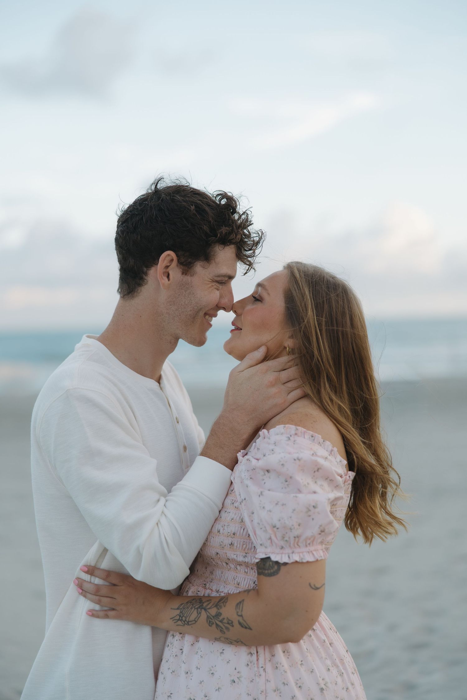 Couple sharing a romantic moment on the beach, man tenderly holding woman's face as they lean in for a kiss.