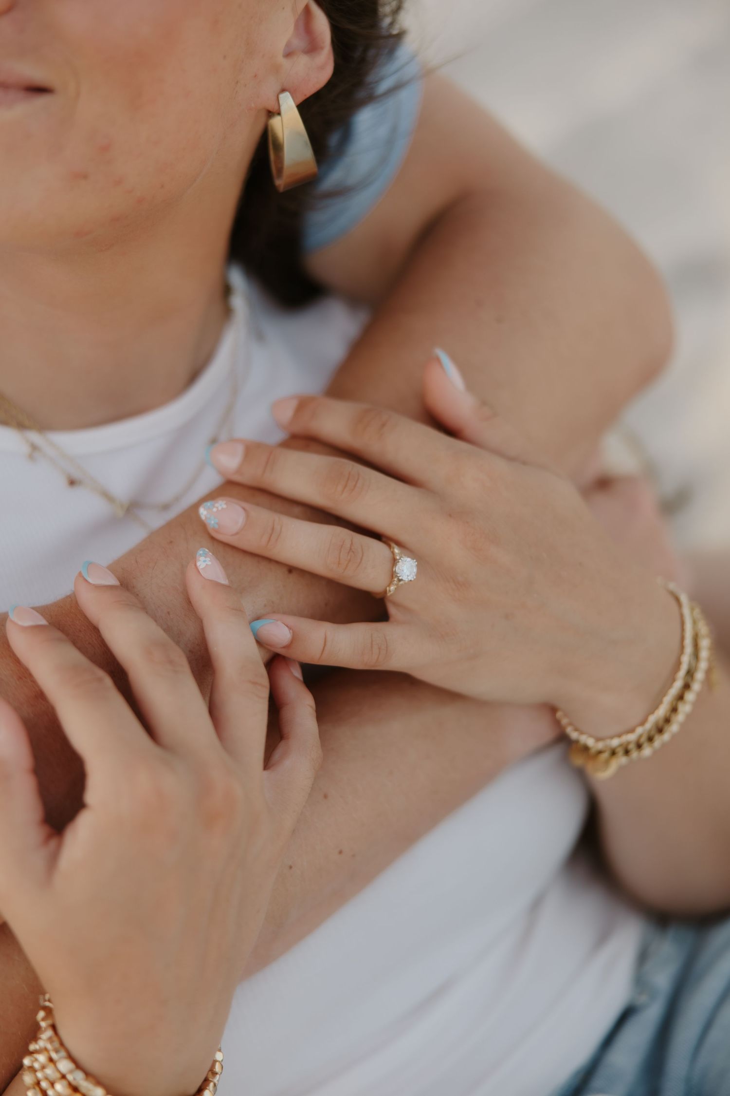 Close-up of an engagement ring on a woman's hand, wearing gold jewelry and bracelets, embracing her partner.
