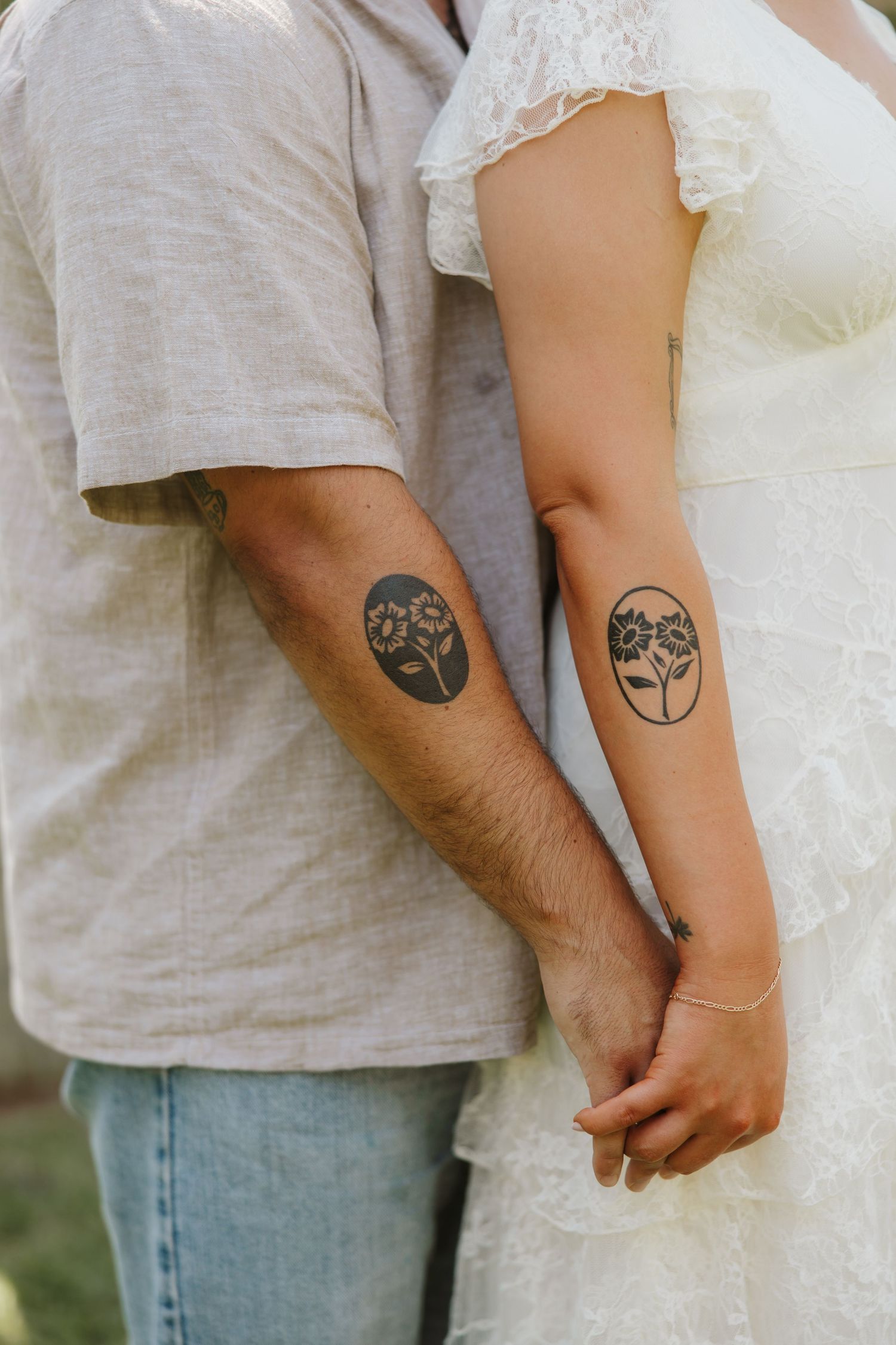 Couple showing matching floral oval tattoos on their forearms, wearing wedding attire.