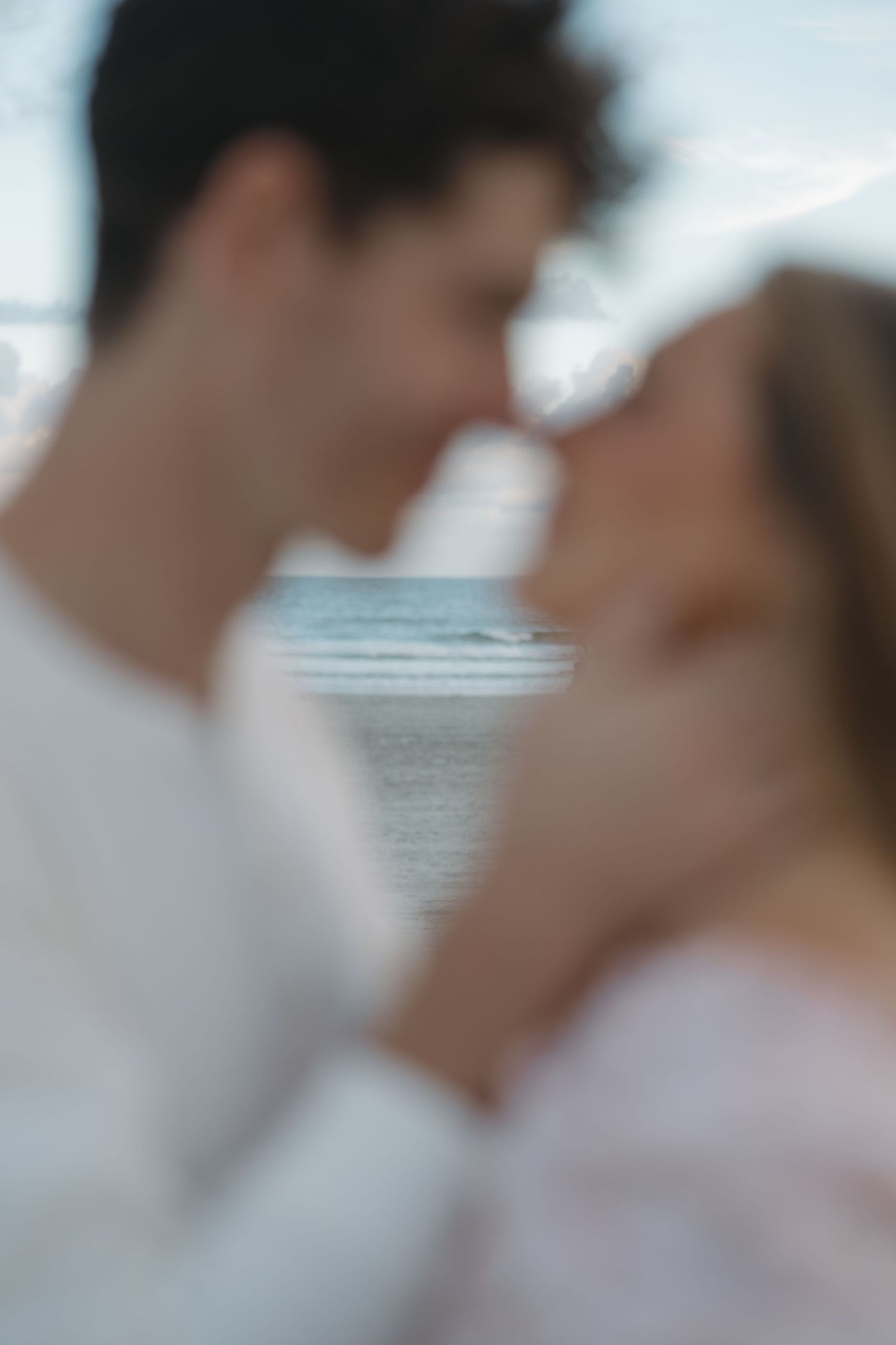 Blurred close-up of a couple sharing a romantic kiss on the beach at dusk.