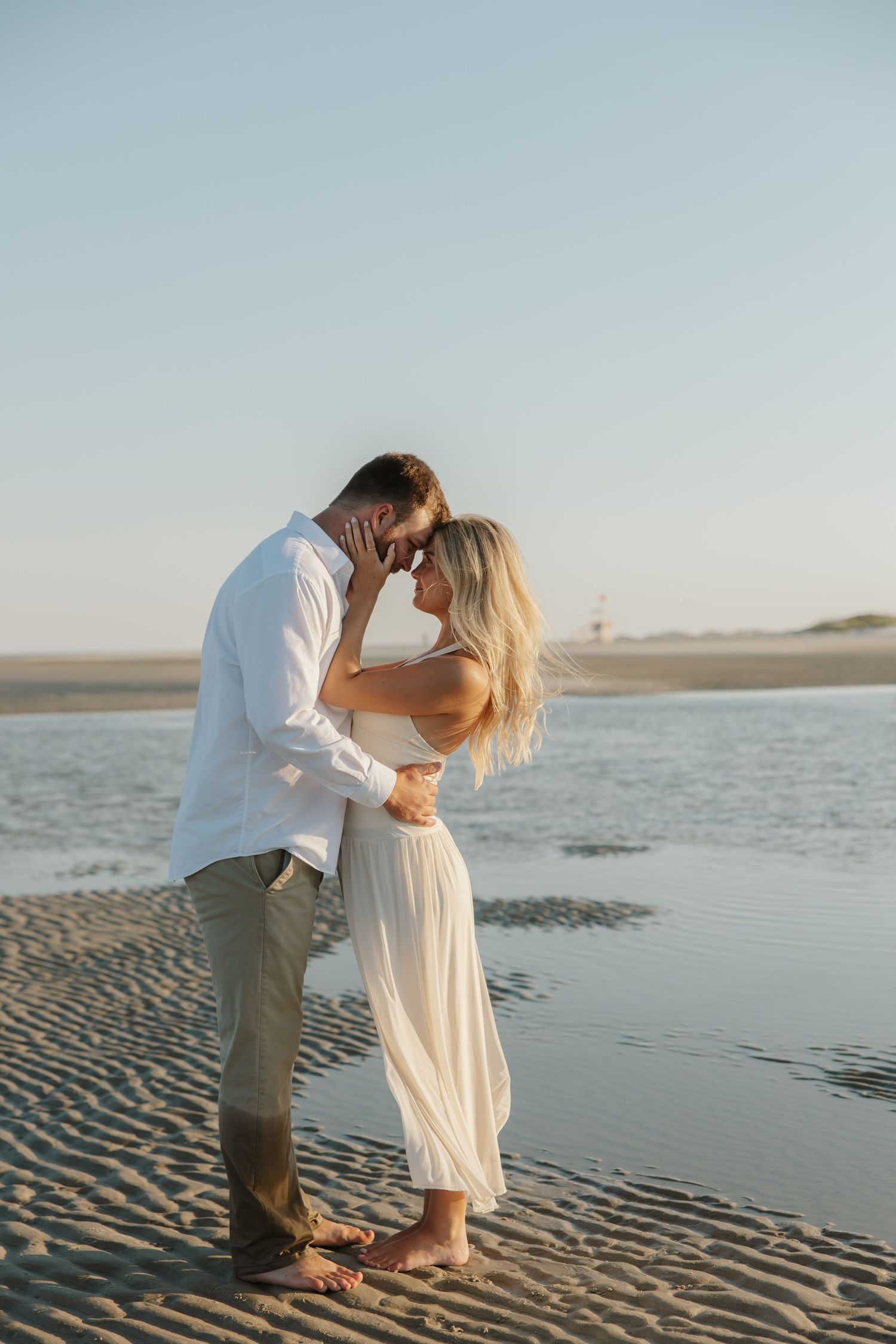 Romantic couple sharing an intimate moment on a sandy beach at golden hour, woman in white dress.