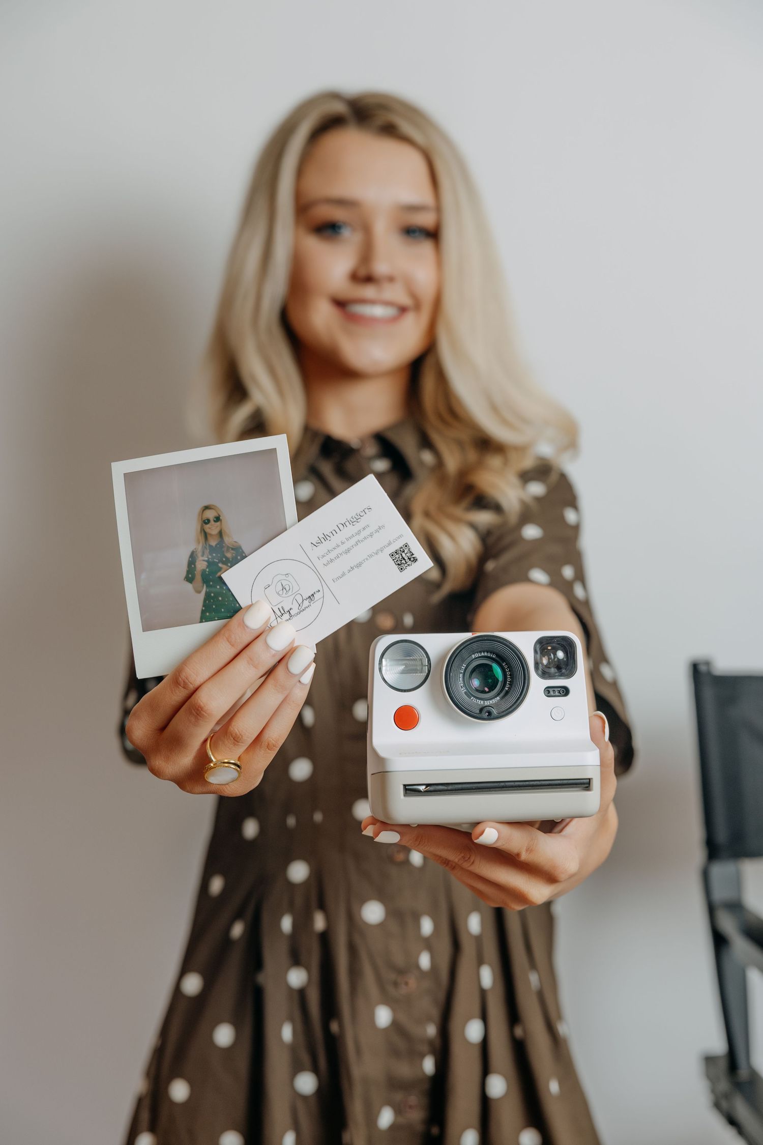 Smiling blonde holding Polaroid camera and instant photo in polka dot dress.