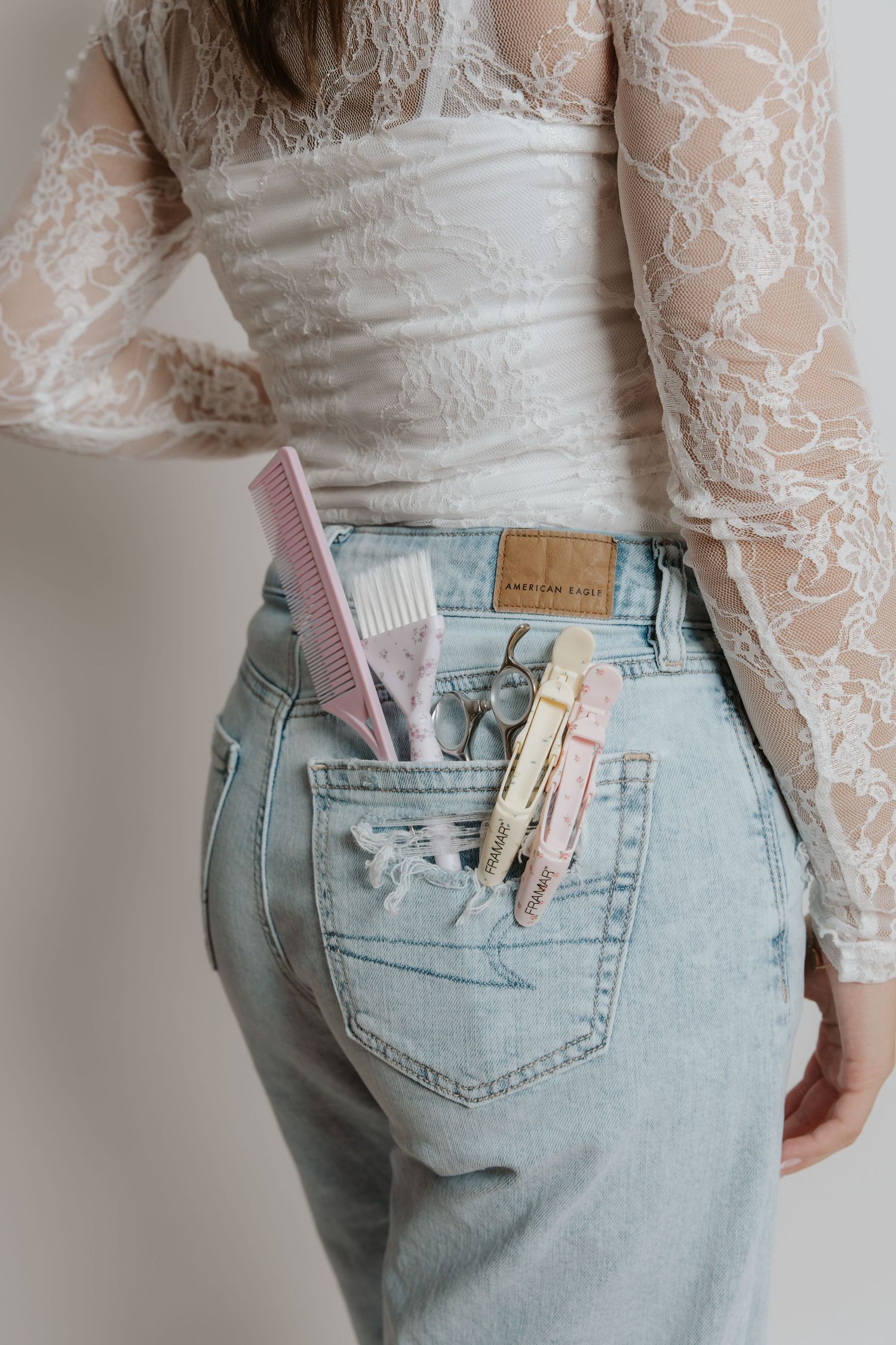 Close-up of hairstylist tools including pink comb and scissors in back pocket of light wash jeans.