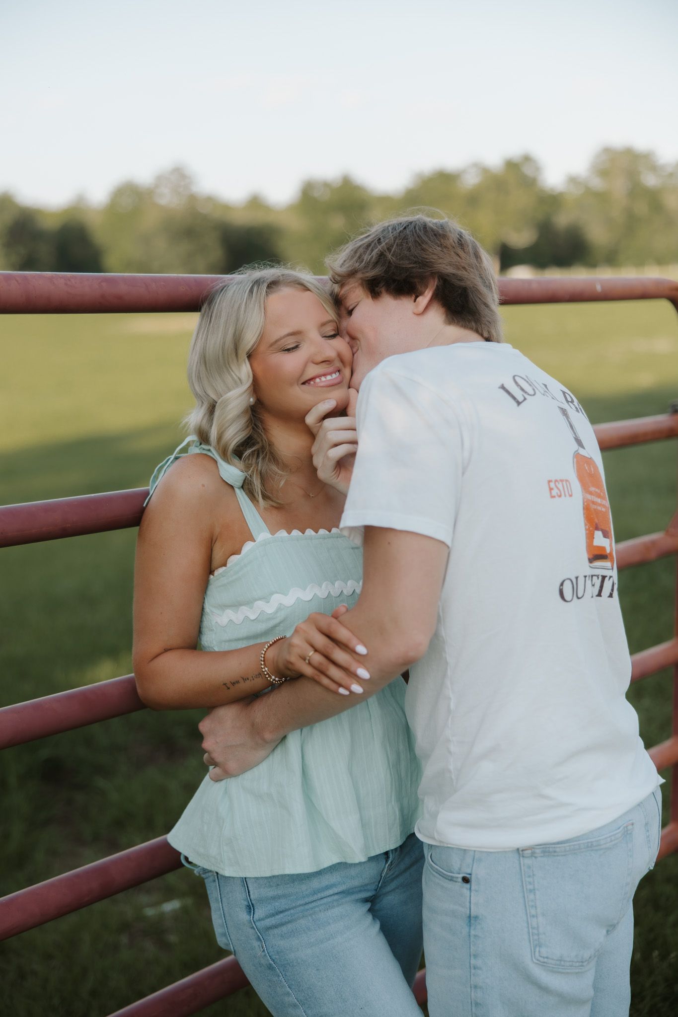 A young couple sharing a tender moment leaning against a red fence outdoors.