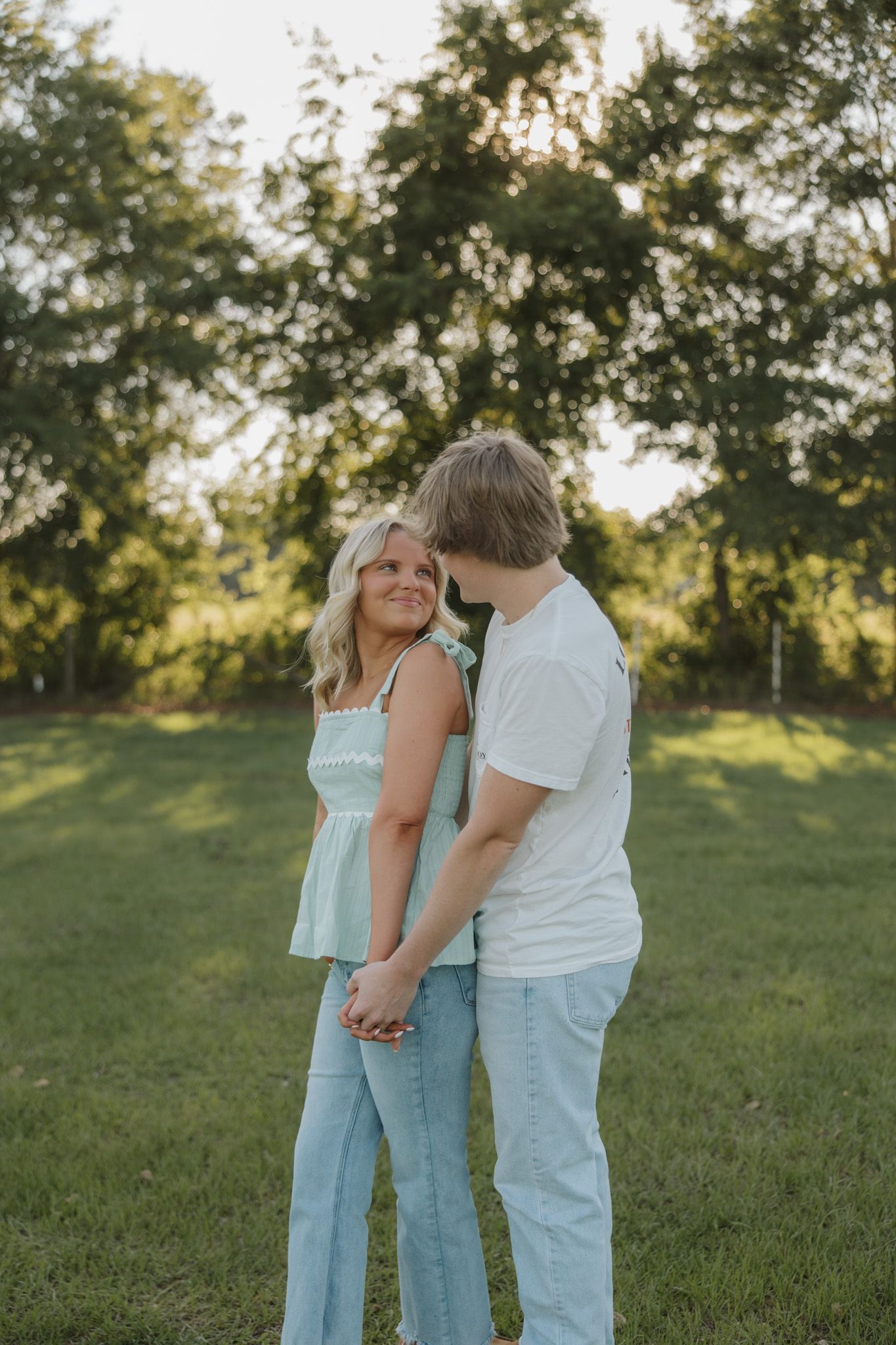 A young couple holds hands and shares a tender moment in a lush green park during golden hour.