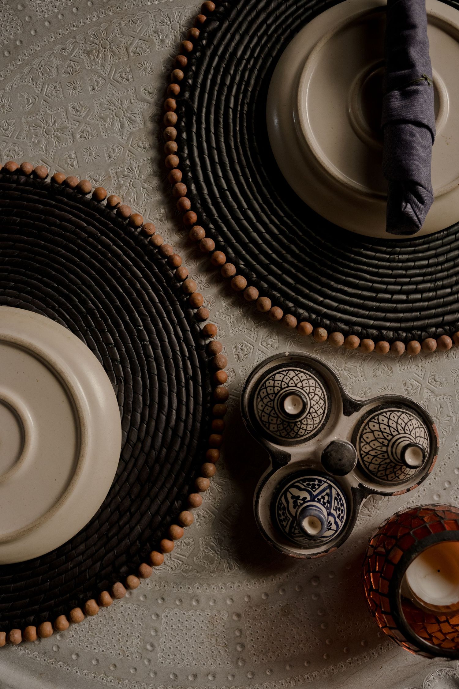 Artistic arrangement of black circular placemats with wooden beads and decorative metal elements.