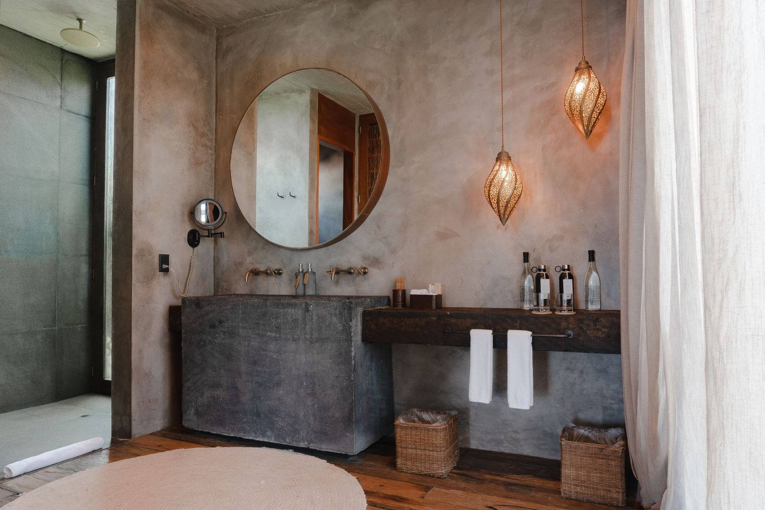 Modern bathroom interior with concrete walls, round mirror, pendant lights and minimalist design features.