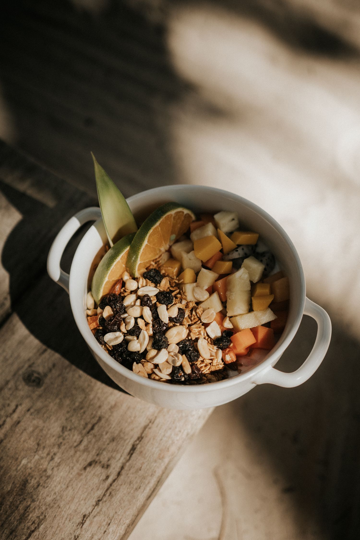 A white ceramic bowl filled with colorful ingredients including chopped vegetables and nuts on a rustic wooden surface.