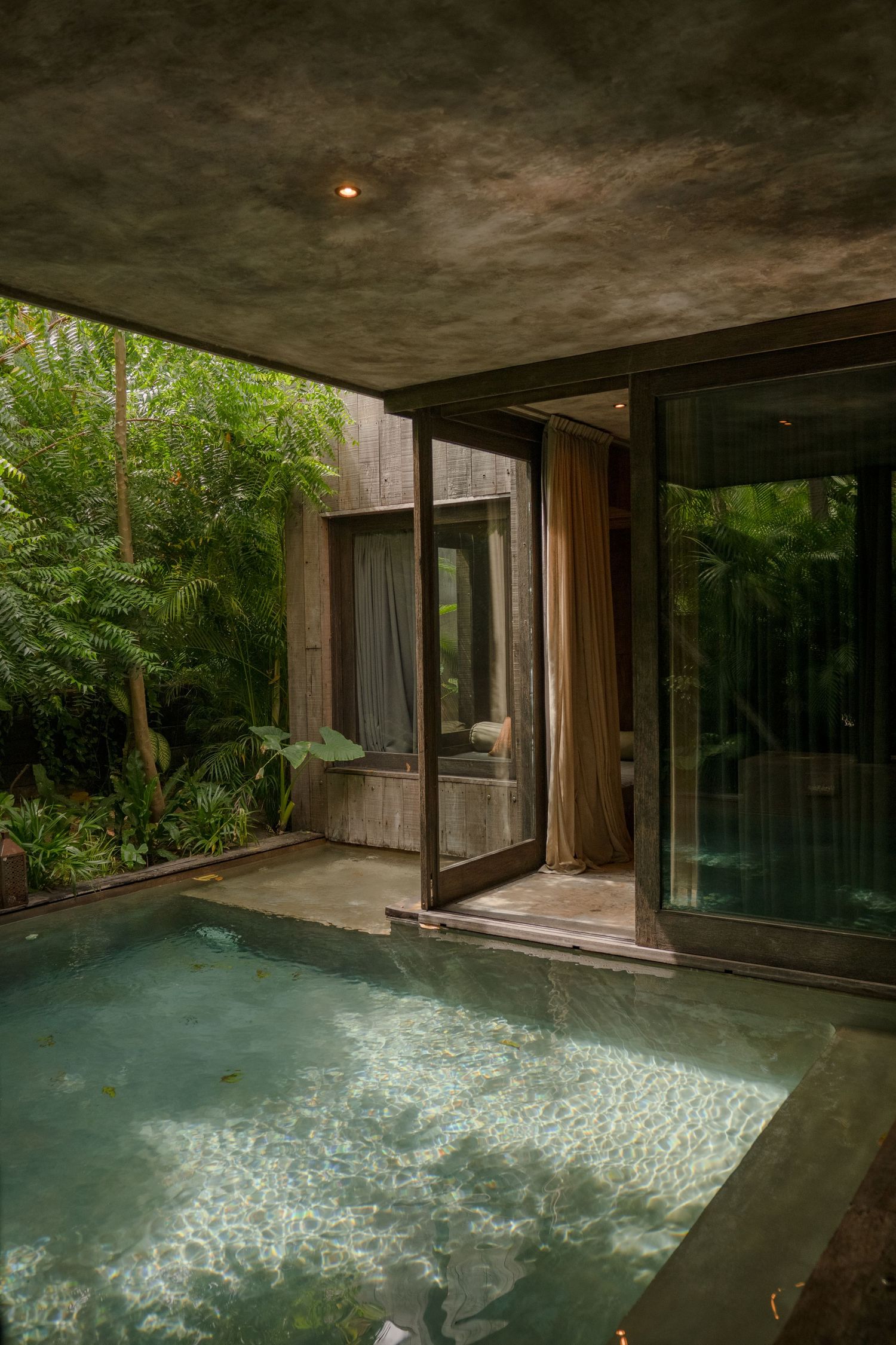A modern indoor pool surrounded by glass walls and lush greenery creating a tranquil spa atmosphere.